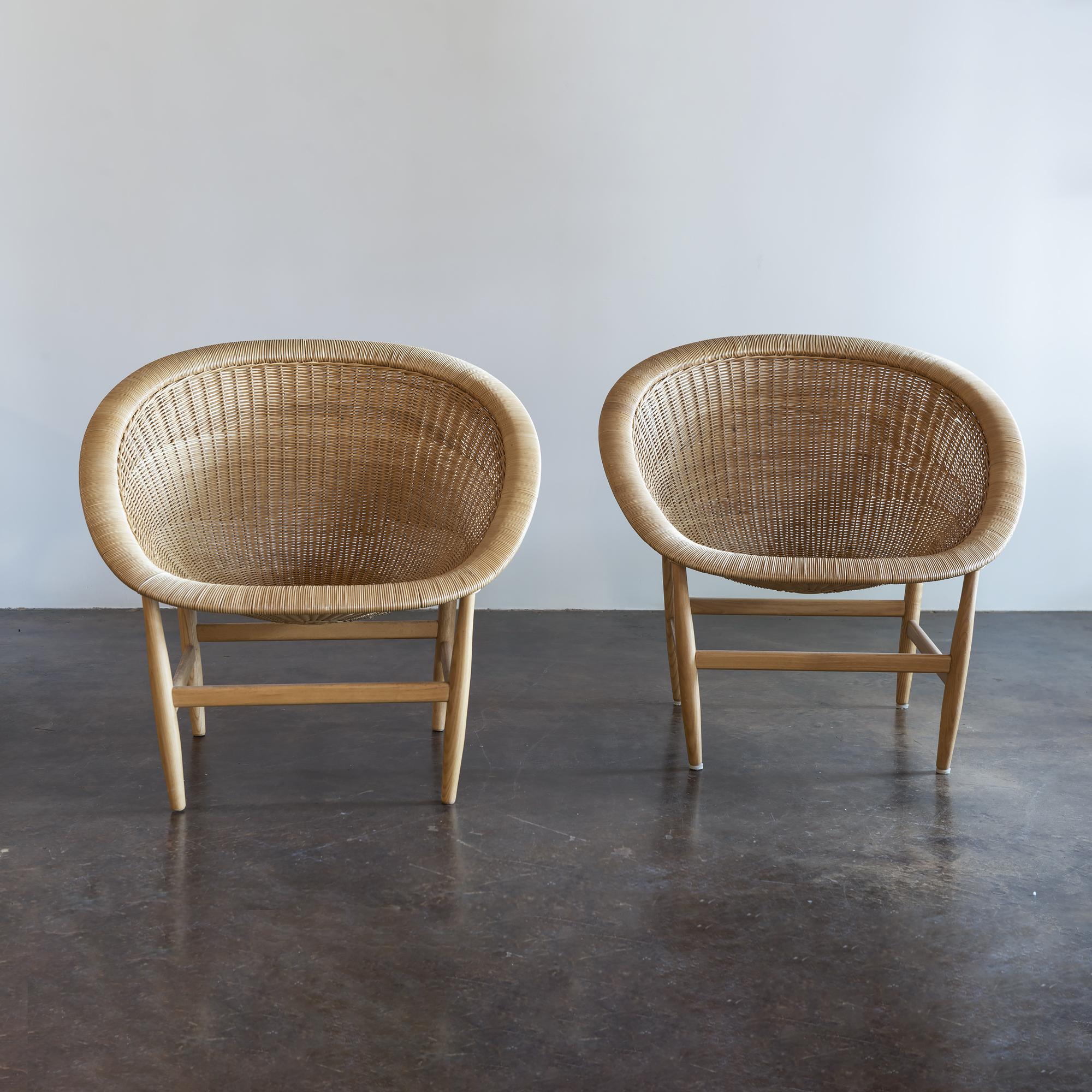 Iconic, organically shaped lounge chairs in hand-braided rattan and ash originally designed by Nanna Ditzel for Ludvig Pontoppidan, Denmark, 1950.  Newer Kettal re-edition.

Pair of chairs comes with new cushions in Place Textiles Mt. Stuart fabric.