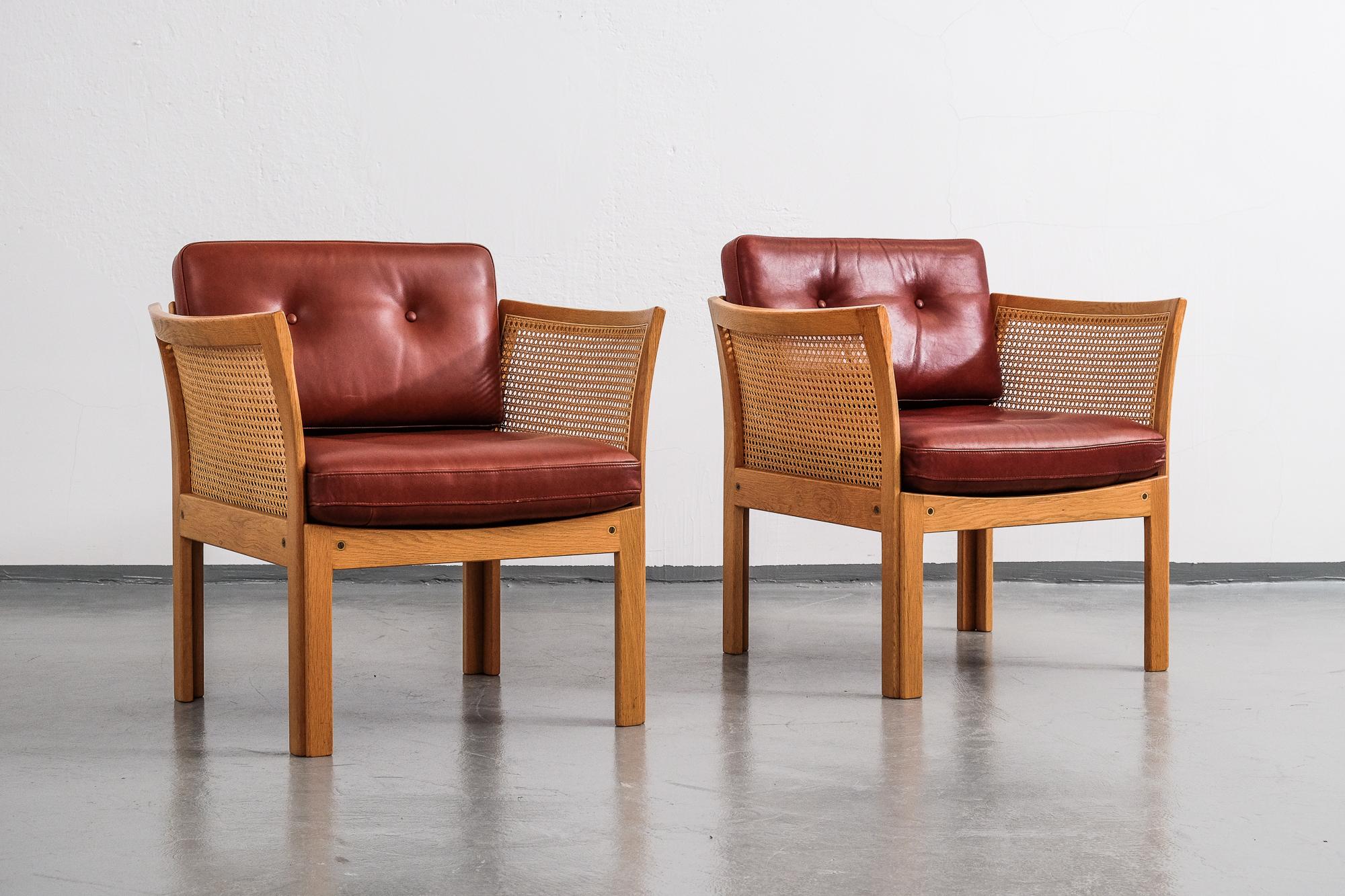 A pair of vintage Illum Wikkelsø 'Plexus' easy chairs in oak and cane.
Loose cushions upholstered in coqnac leather.

Produced by C.F. Christensen.