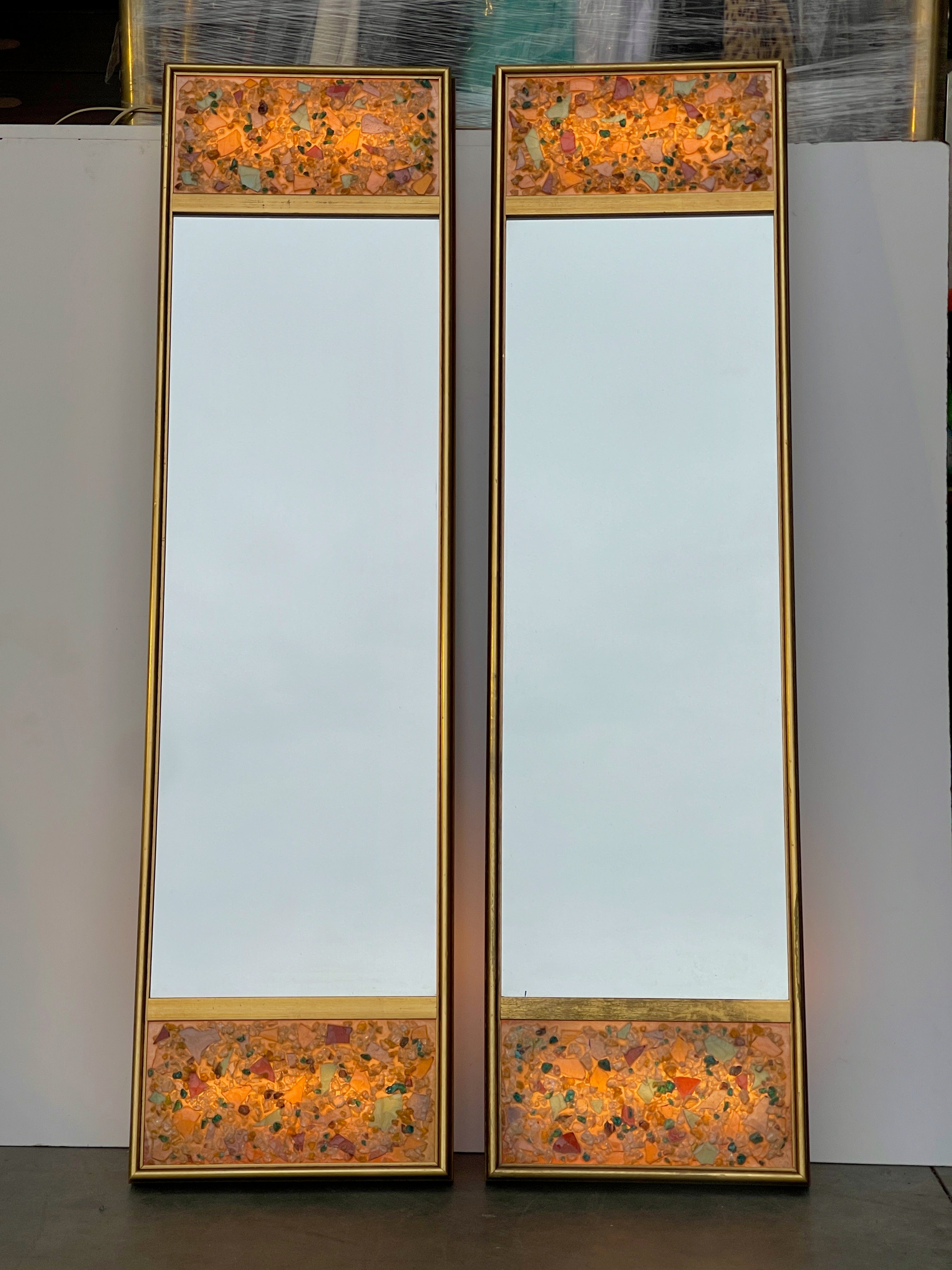 Pair of Hollywood Regency illuminated wall mirrors in gilt wood shadow box frames with inset panels of colored acrylic resin gemstones crafted to look like crushed glass cullet.
From an outrageously over-the-top period Hollywood Regency decorated