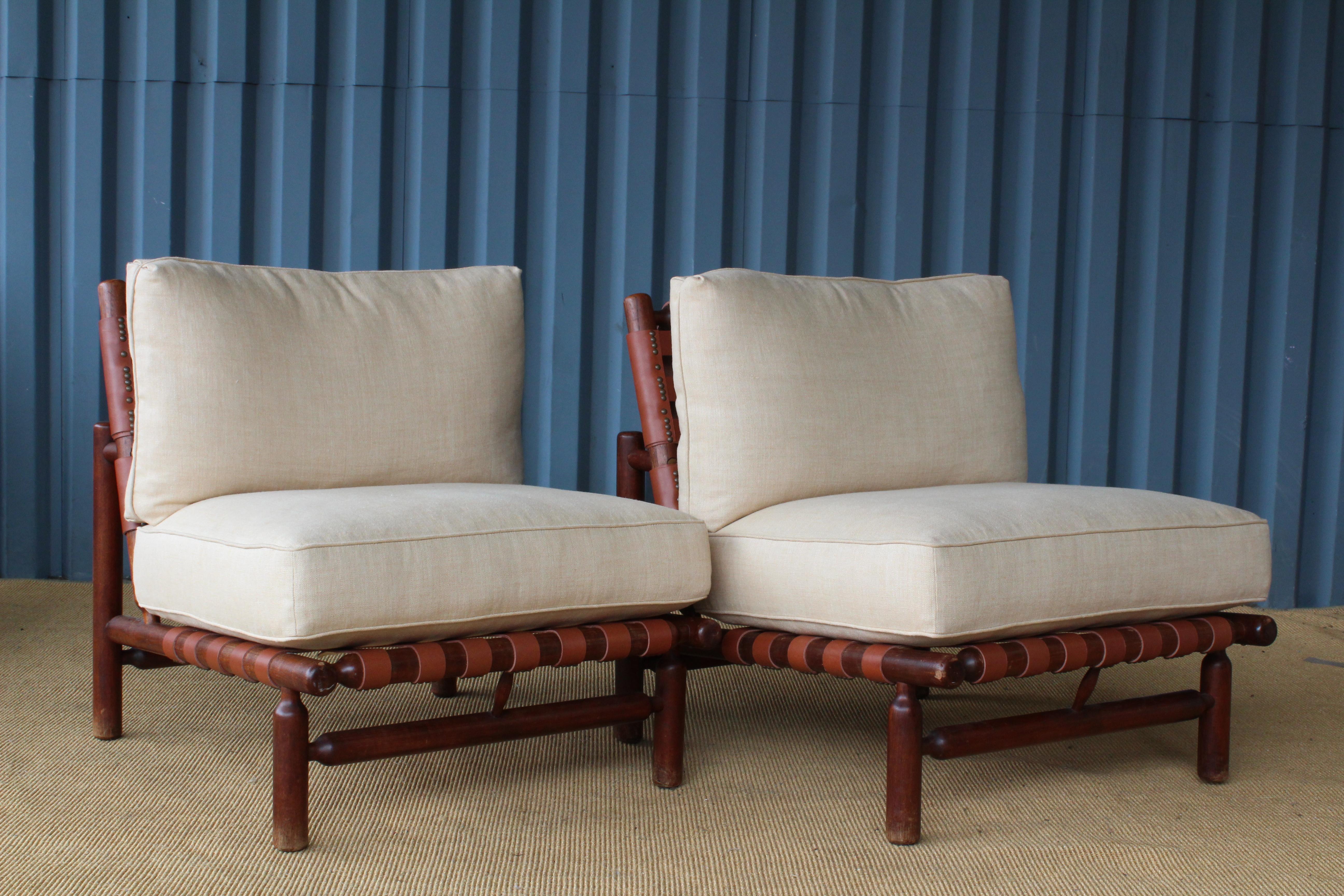 Pair of lounge chairs designed by Ilmari Tapiovaara for Esposizione La Permanente Mobili, Italy, 1957. The pair have new leather straps and new linen cushions. Walnut frames show age appropriate signs of wear.