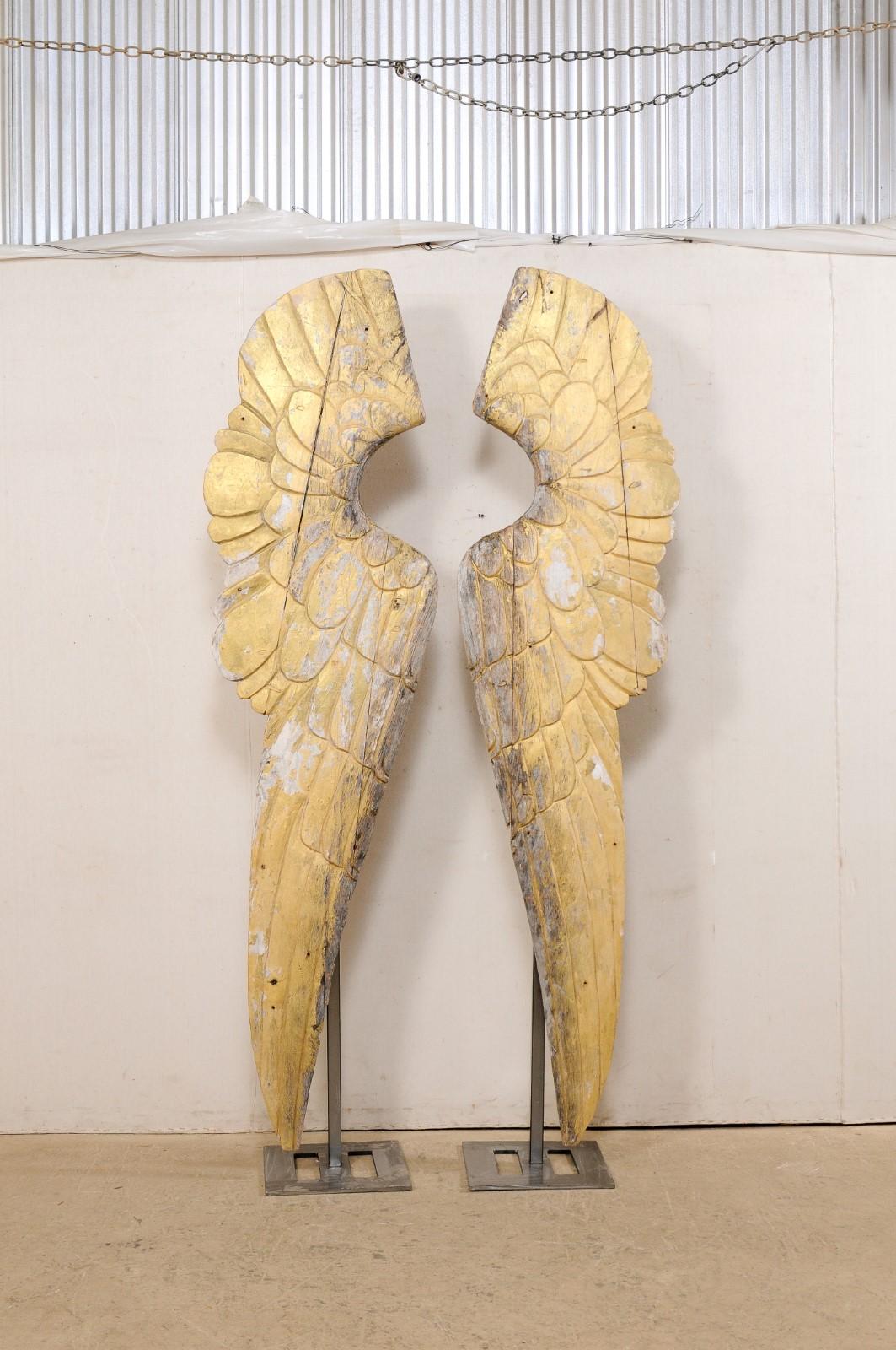 A very large pair of European carved and gilt wood wings on custom iron stands. This pair of vintage angel wings from Europe have been hand-carved of wood and retain much of their original gilt finish. They have a lovely patina, and are each