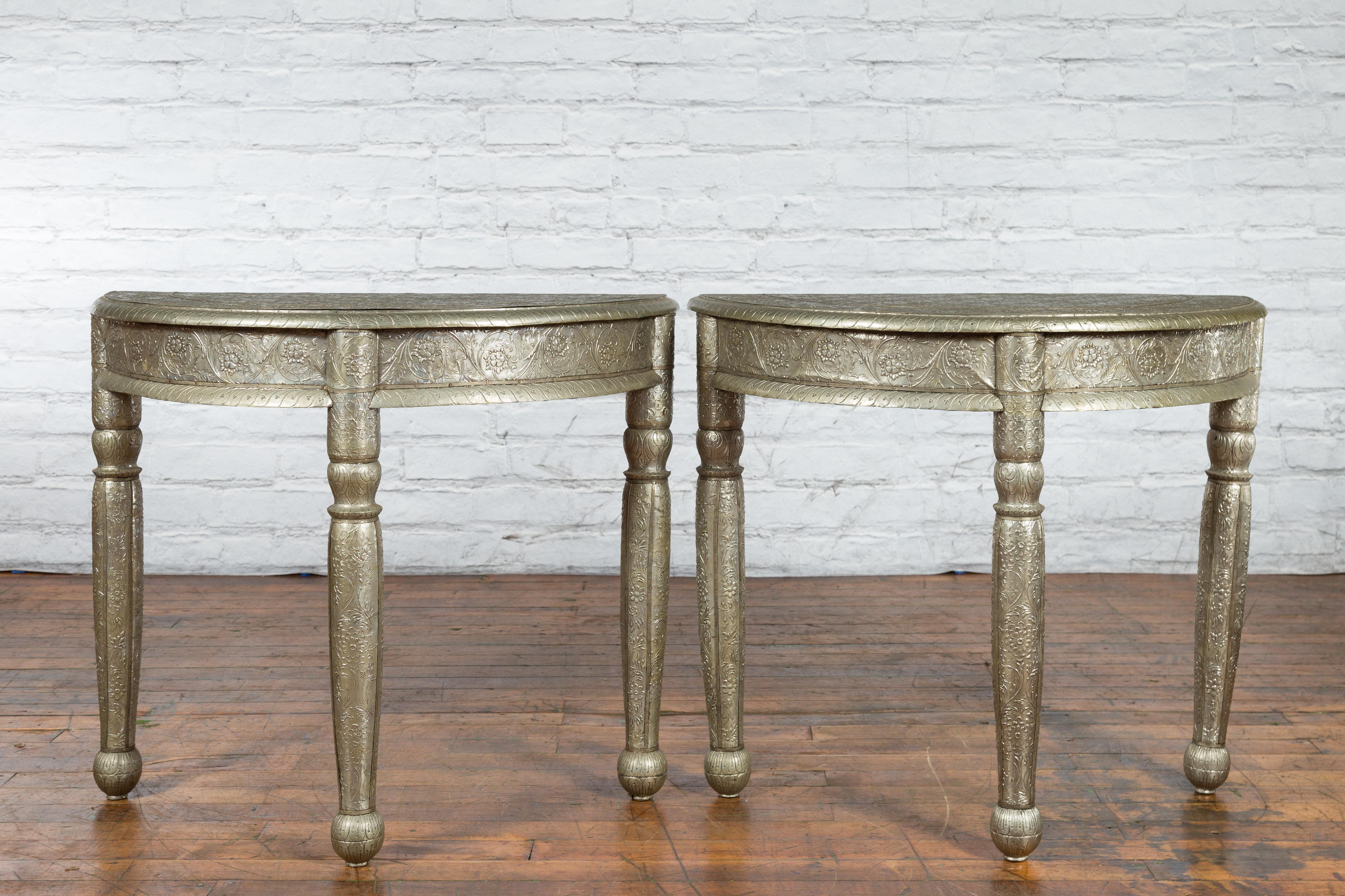 A pair of antique Indian repoussé demi-lune tables from the 19th century, with floral arabesques and made of metal sheathing over wood. Created in India during the 19th century, each of this pair of demilune tables features a semi-circular top