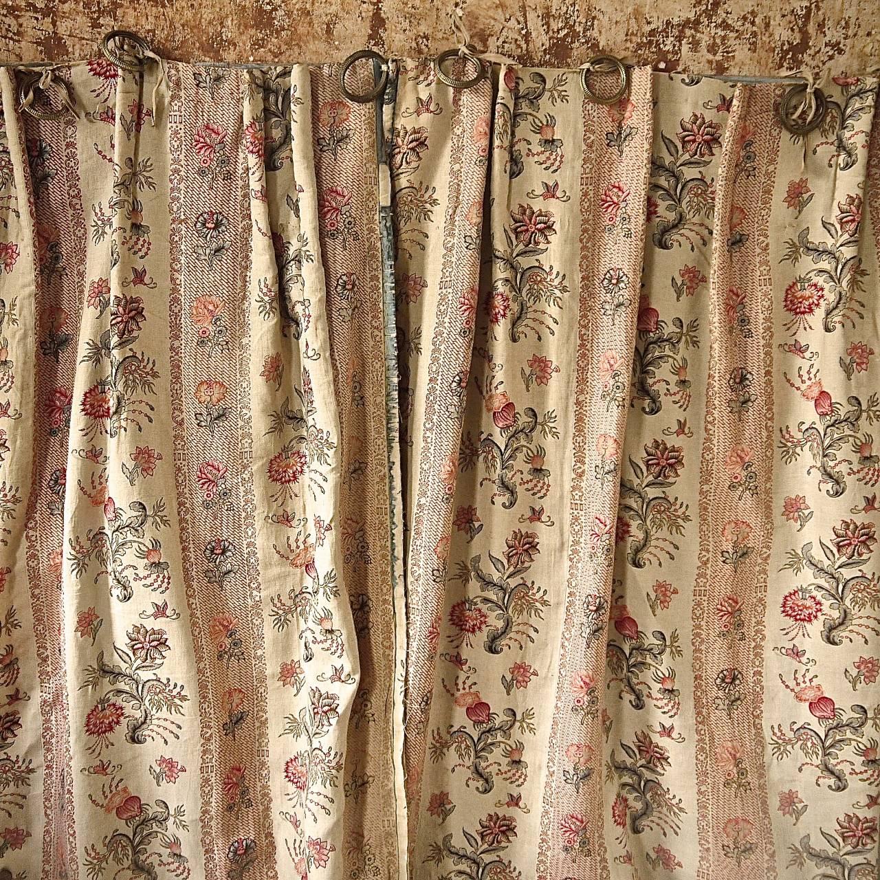 Pair of French late 19th century linen curtains printed with a stylised Indienne type design of flowers and patterned columns in soft rasberry and a greyish blue. Finished with a blue moire silk trim that is missing in many places and with its