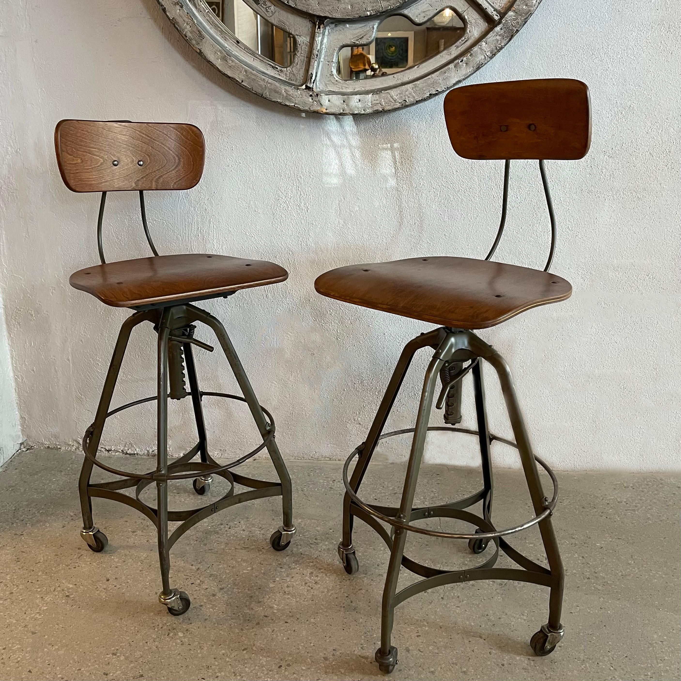Coppia di sgabelli industriali da disegno degli anni '40 di Toledo Metal Furniture Co. con basi regolabili in altezza, in acciaio verniciato grigio-verde, telaio ad A con multistrato d'acero piegato, sedili e schienali girevoli. Gli sgabelli sono