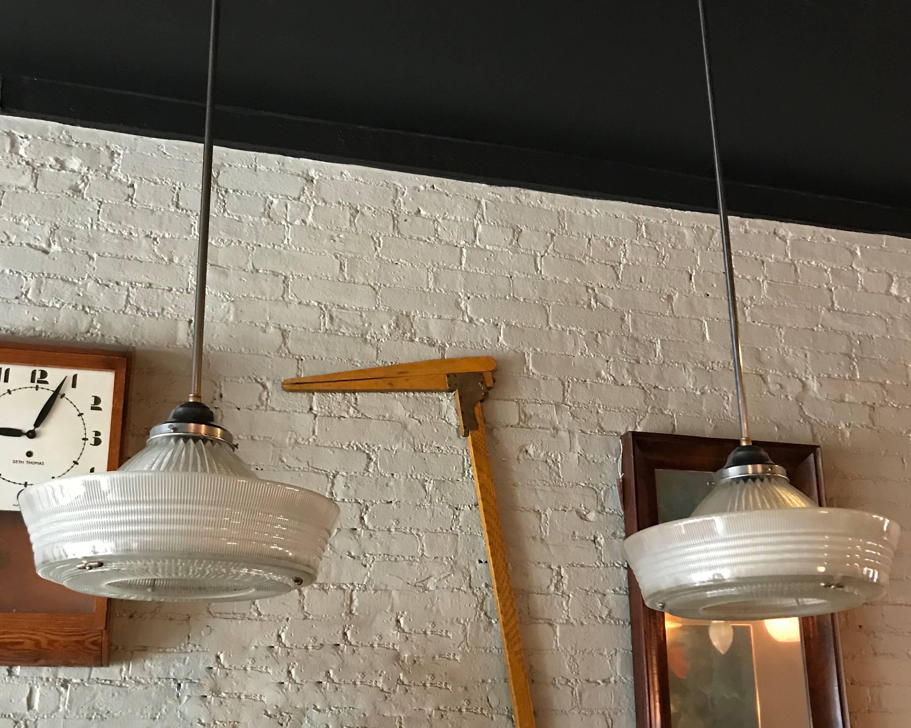 Pair of monumental, rare, Holophane pendant lights feature three intricate, prismatic patterns on their dome, side and bottom of brims with steel fitters and stems are newly wired to accept a 300 watt bulb each. Measures: Height to top of fitter is