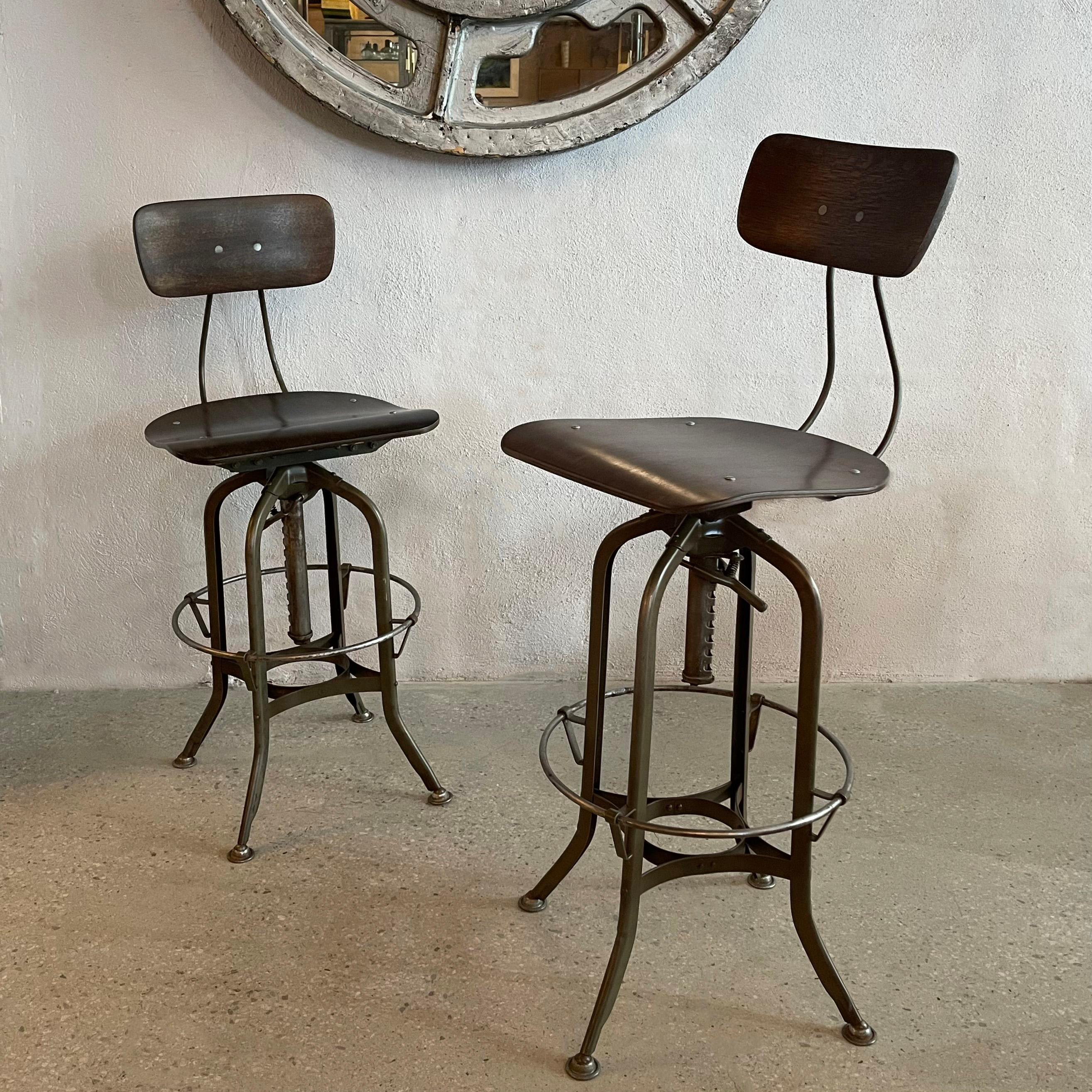 Pair of iconic, industrial drafting stools by Toledo Metal Furniture Co. circa 1940's feature height adjustable, steel star bases with bent maple ply, swivel seats and backs. One stool is height adjustable from 28 - 33 inches and the other adjusts