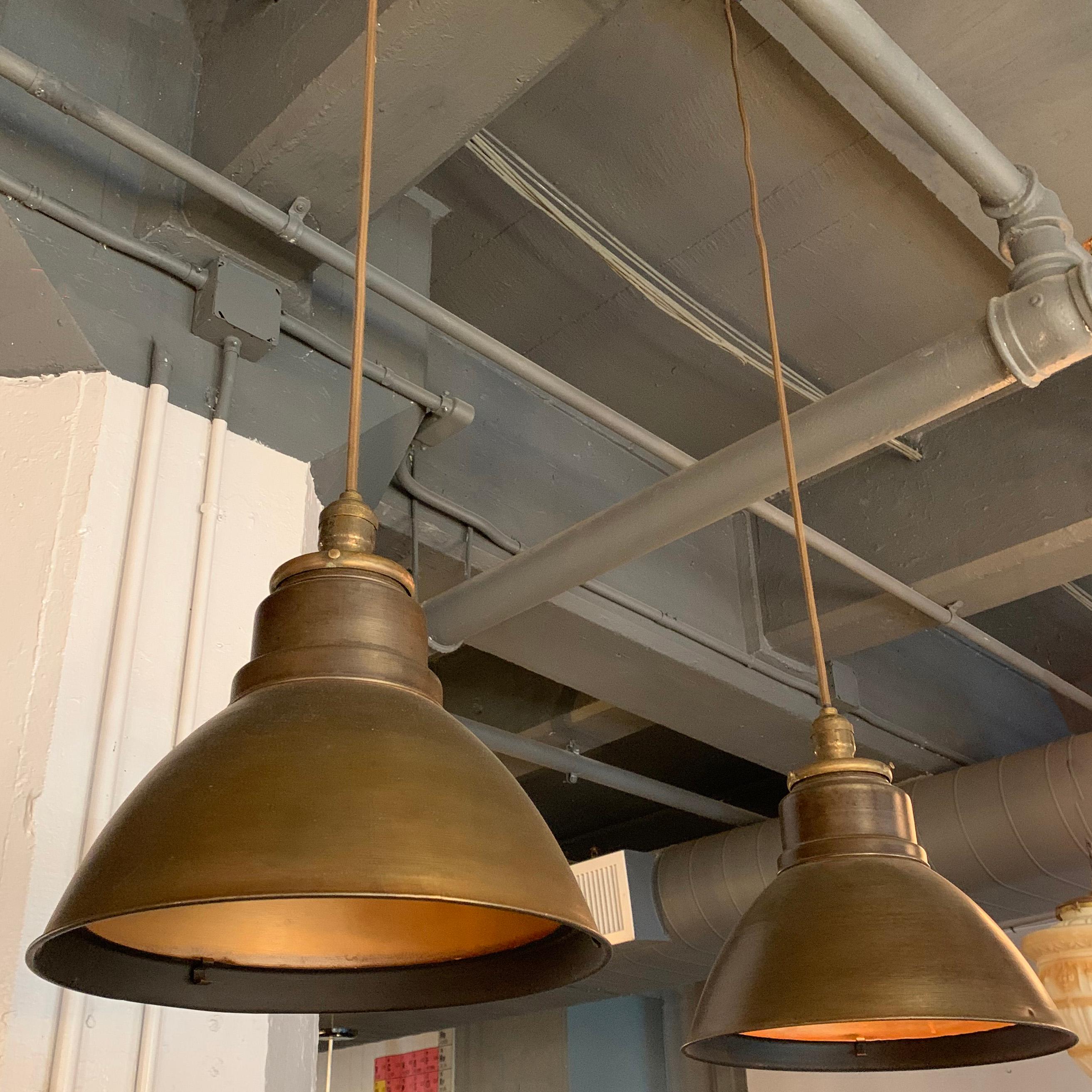 Pair of industrial factory pendants lights feature steel dome shades in a gunmetal exterior finish with reflective brass-toned interiors. The pendants are newly wired with 44 inches of brown cloth cord to accept medium socket bulbs up to 200 watts.