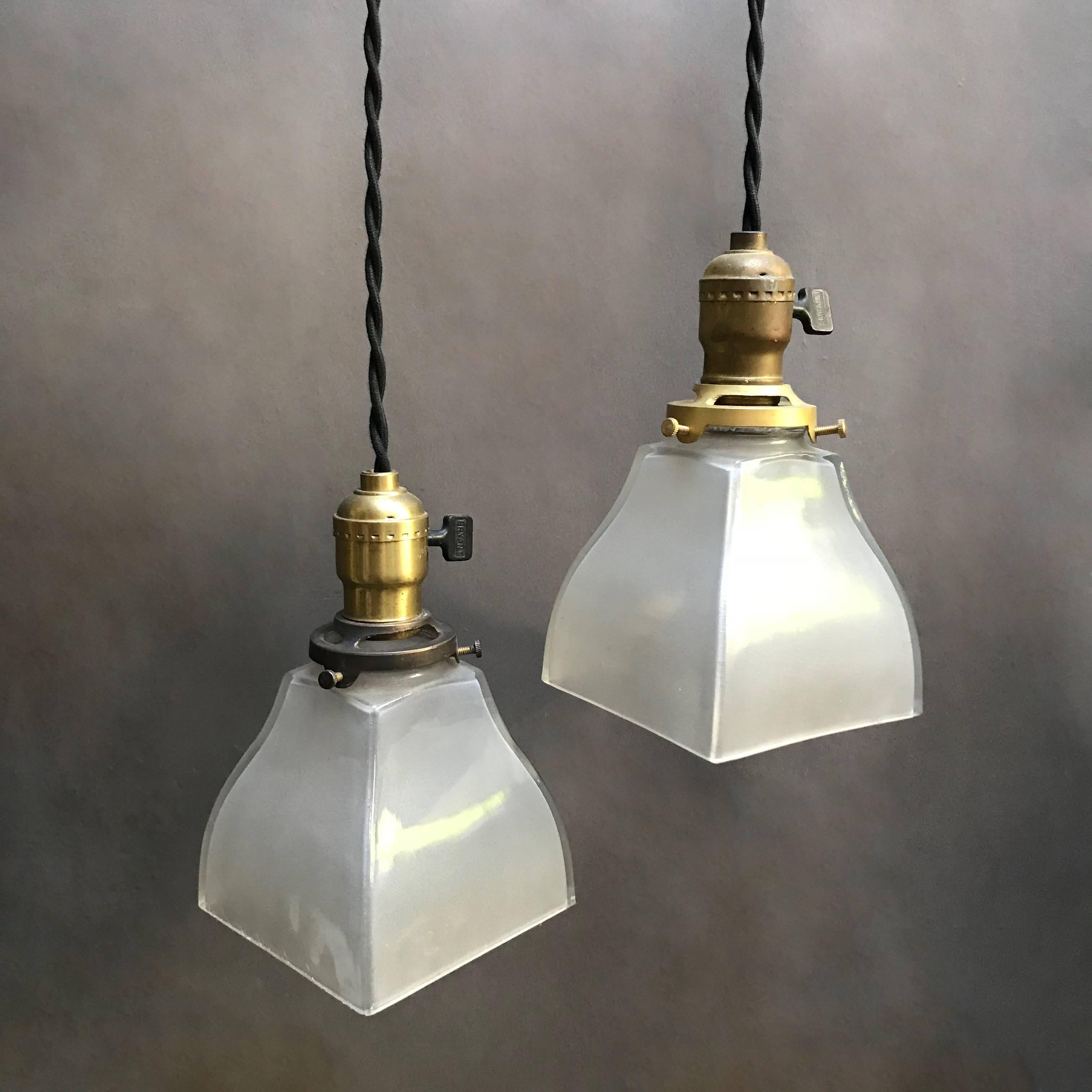 Pair of industrial pendant lights feature squared, open, frosted glass shades with brass switch fitters are newly wired with 40 inches of braided black cloth cord to accept up to 150 watt bulbs each.