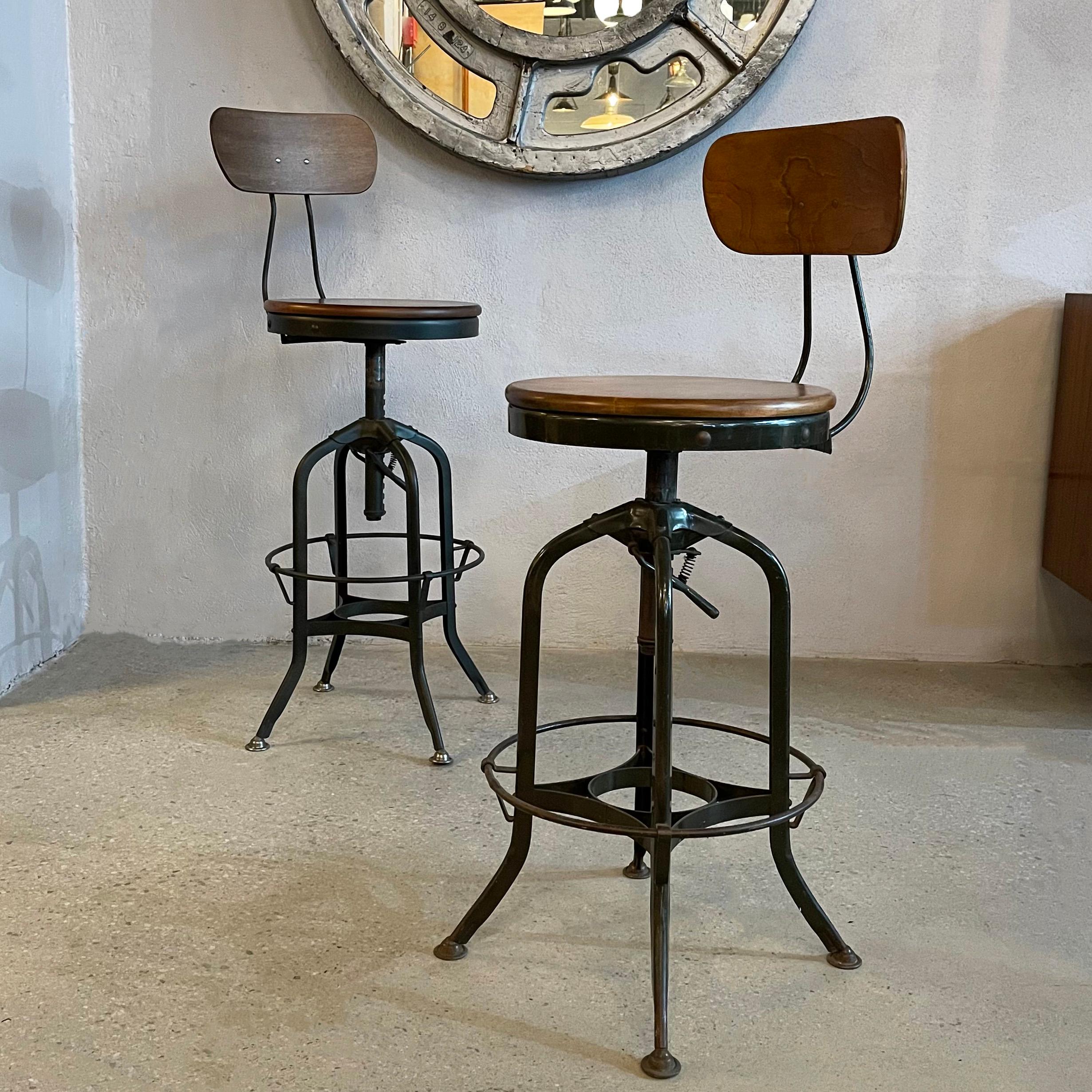 Pair of industrial, swivel, drafting stools by Toledo Metal Furniture Co., circa 1940's feature muted gray green, painted metal frames with maple seats and backs. The stools are height adjustable incrementally from 25 - 33 inches making them