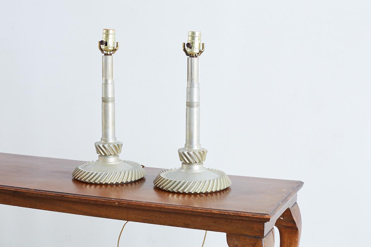 Lustrous pair of industrial machine age gear or cogwheel table lamps. Large mechanical gear parts having teeth on the main shaft and bottom edge converted to table lamps. These lamps feature a rich, lustrous finish like they are made of platinum