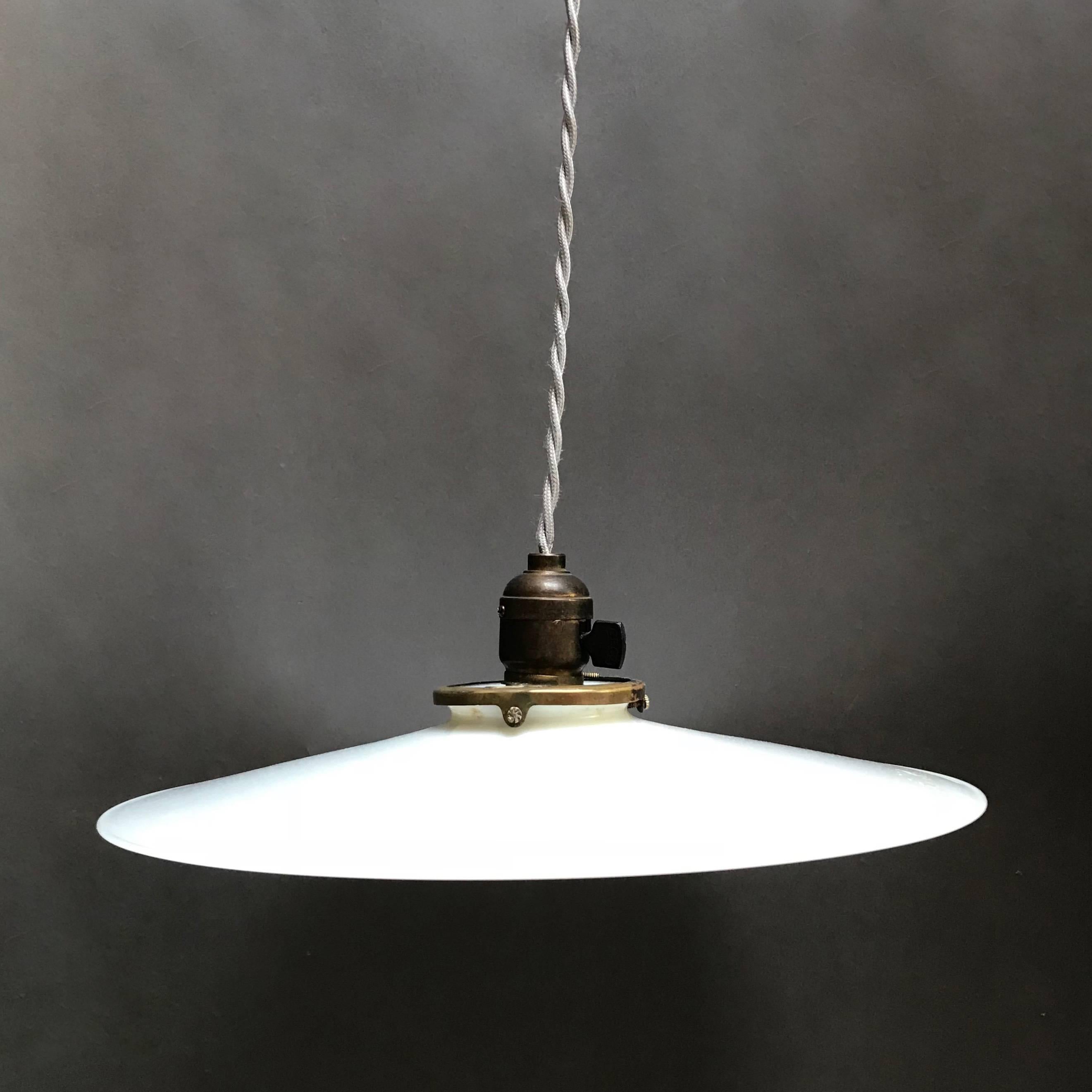 Pair of industrial pendant lights feature 13 inch, milk glass disc shades with open brass fitters are newly wired with 40 inches of braided gray cloth cord to accept up to 150 watt bulbs each.