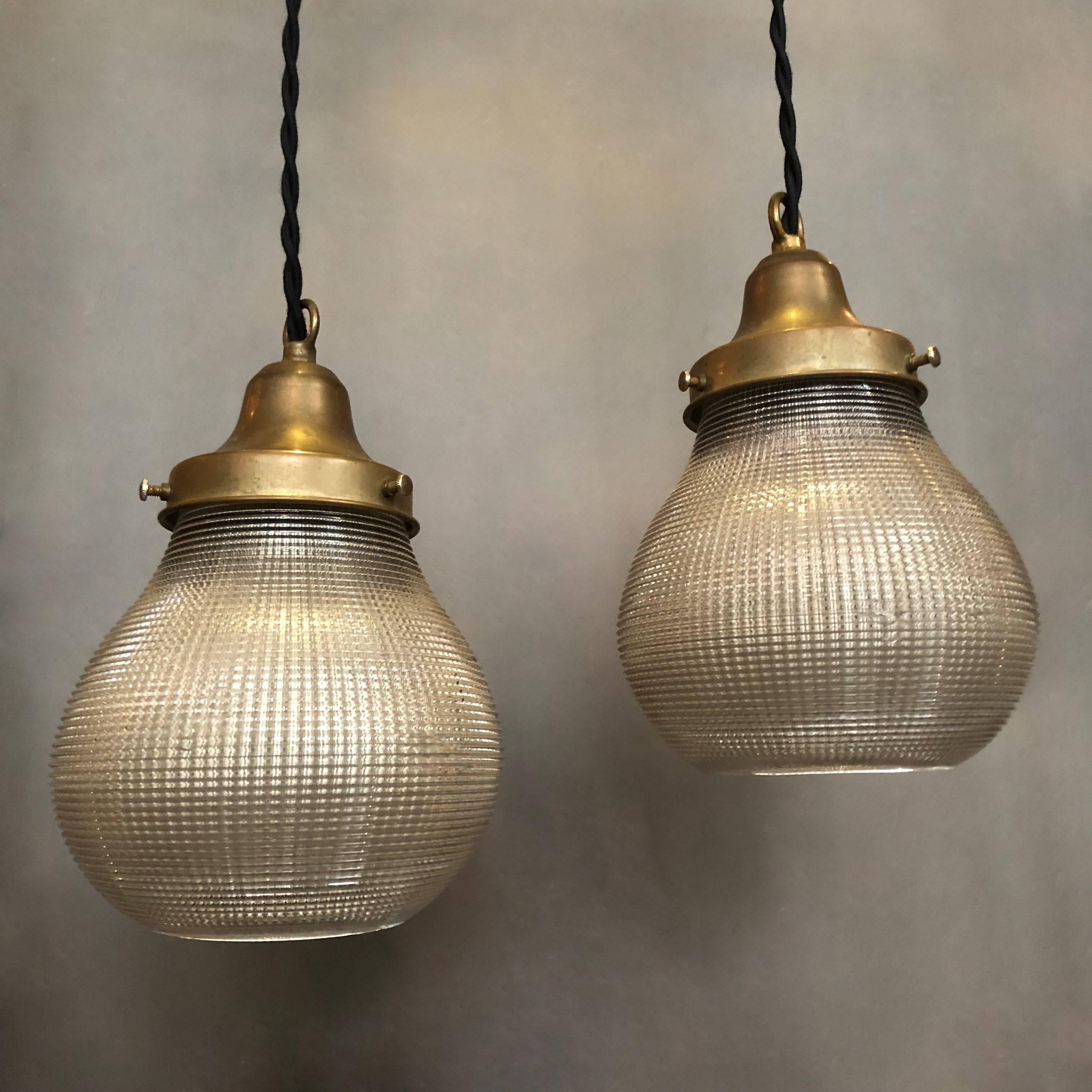 Pair of Industrial pendant lights feature pear-shaped, prismatic Holophane glass shades with open bottom and brass fitters are newly wired with 48in. of braided cloth cord to accept 150 watts bulbs. Two pairs are available.