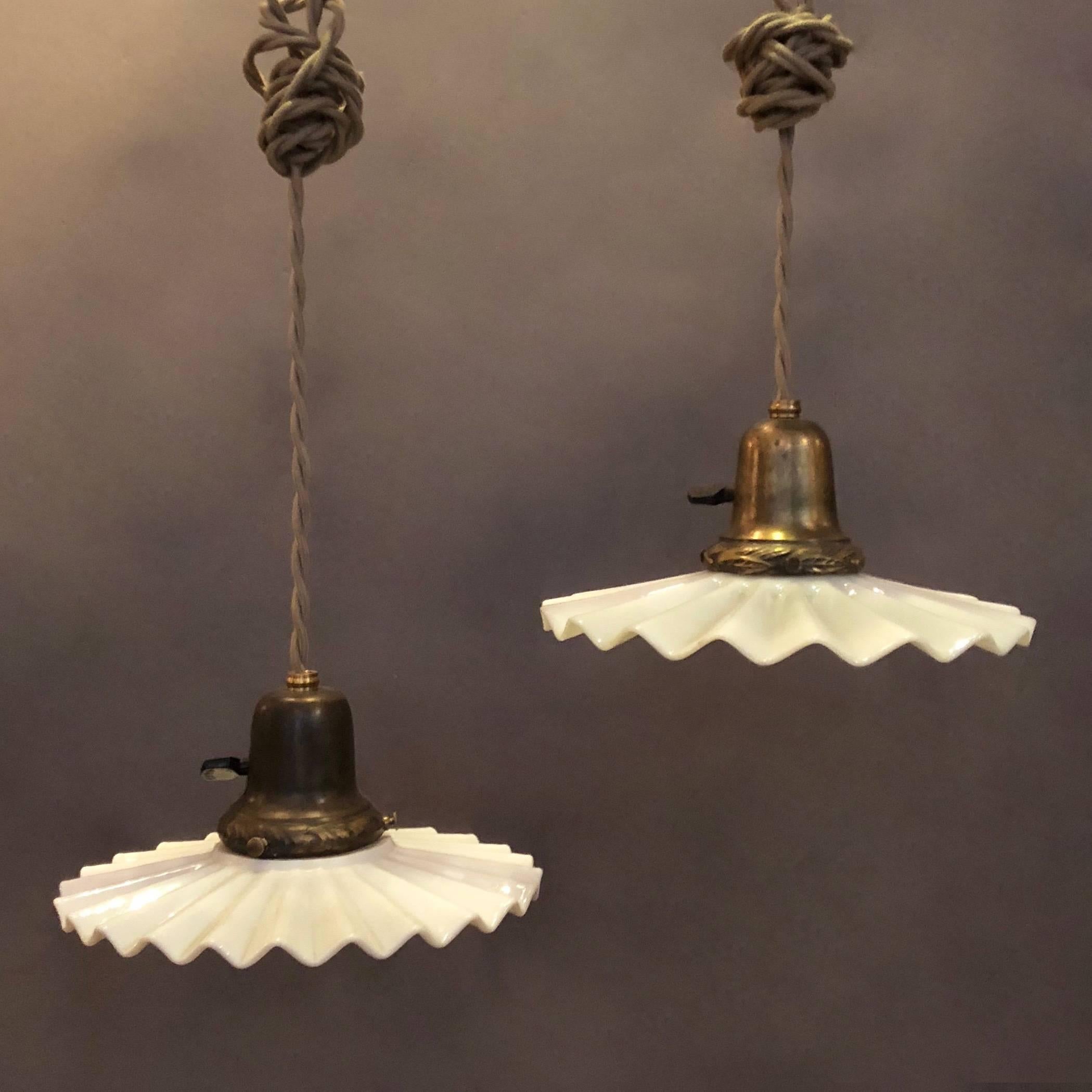 Pair of Industrial, milk glass pendant lights feature ruffled disc shades with brass fitters that are newly wired with 48in. of braided cloth cord to accept 150 watt bulbs. We more ruffle milk glass pendant lights in various sizes.