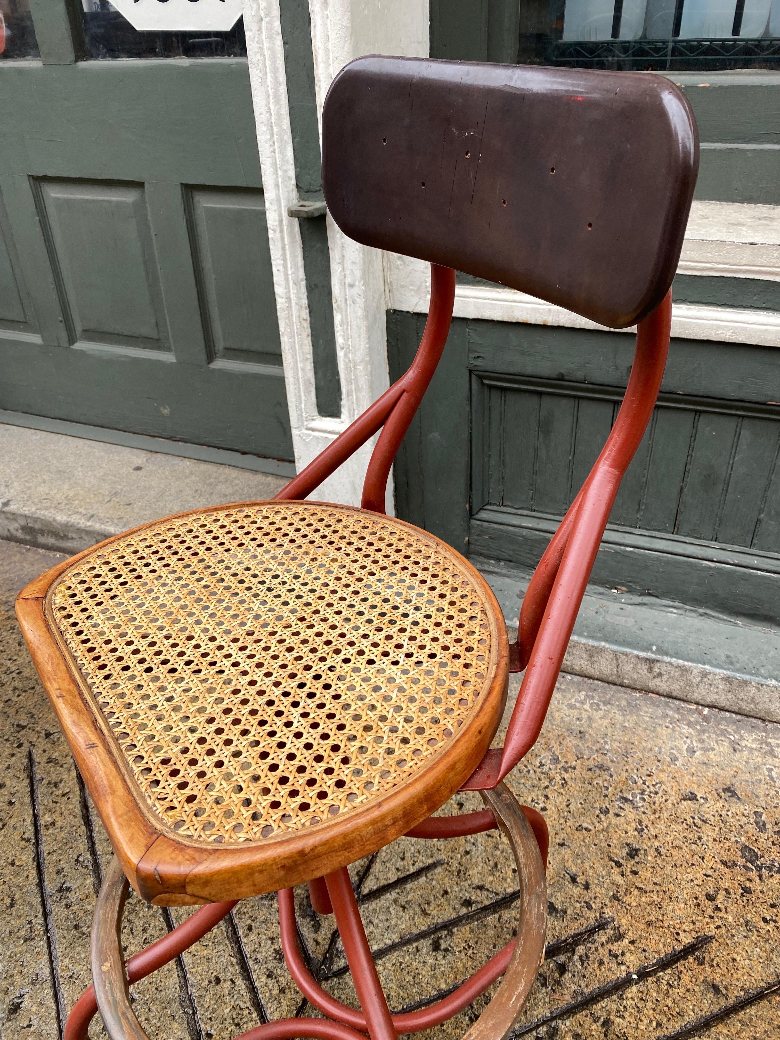 Pair of industrial drafting stools. Cane Seats with a bakelite tilting back rest. Metal frame with wood Circular feet rests. Looks like they were fixed up within last 10-15 years? Frames painted and new cane. Unusual look and ready to go! Wood rings