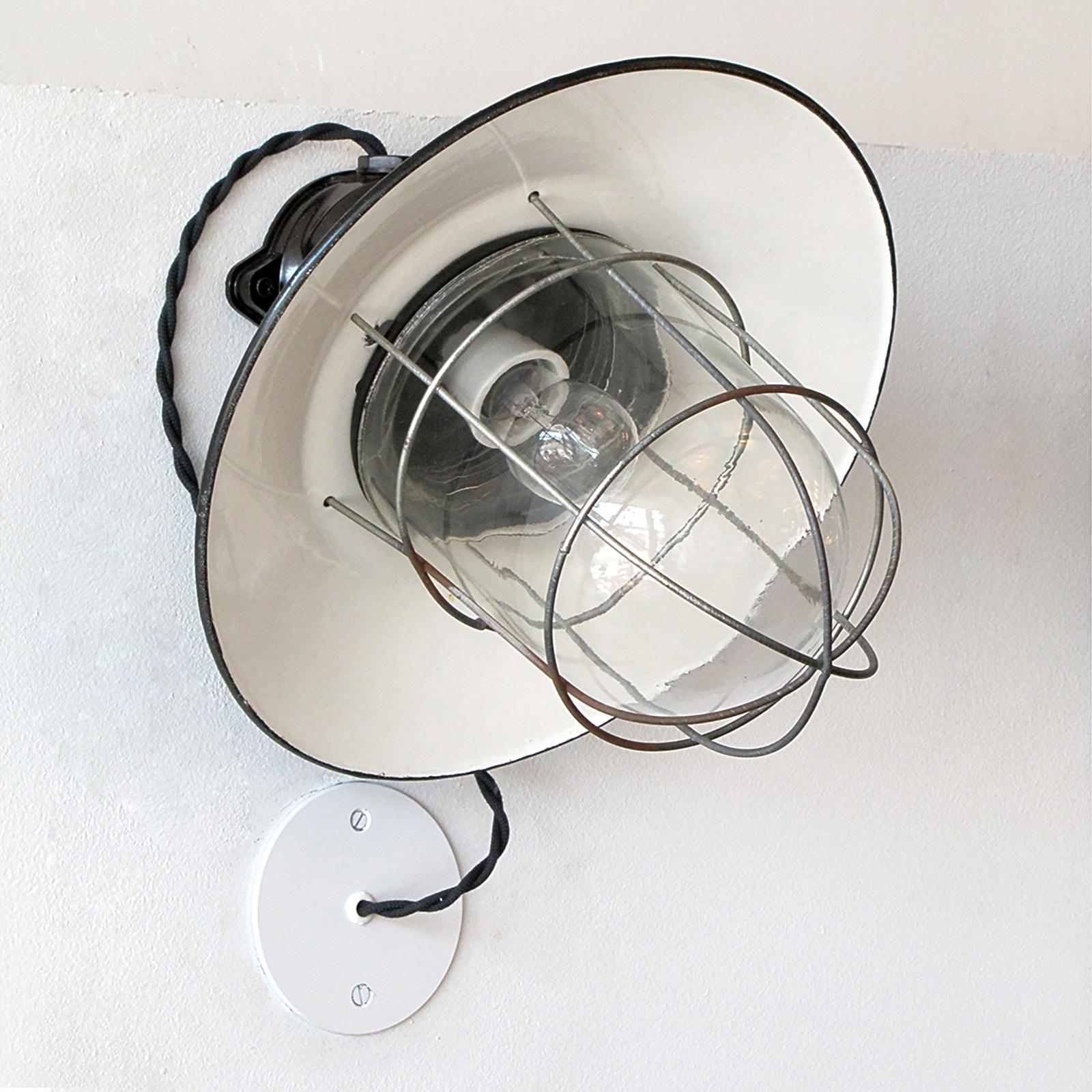 Great pair of German Industrial wall lights with bakelite housings, enameled metal shades and a metal cages enveloping glass domes, currently wired with external j-box covers, wired for US standards, one E27 socket per fixture, max. wattage 100w,