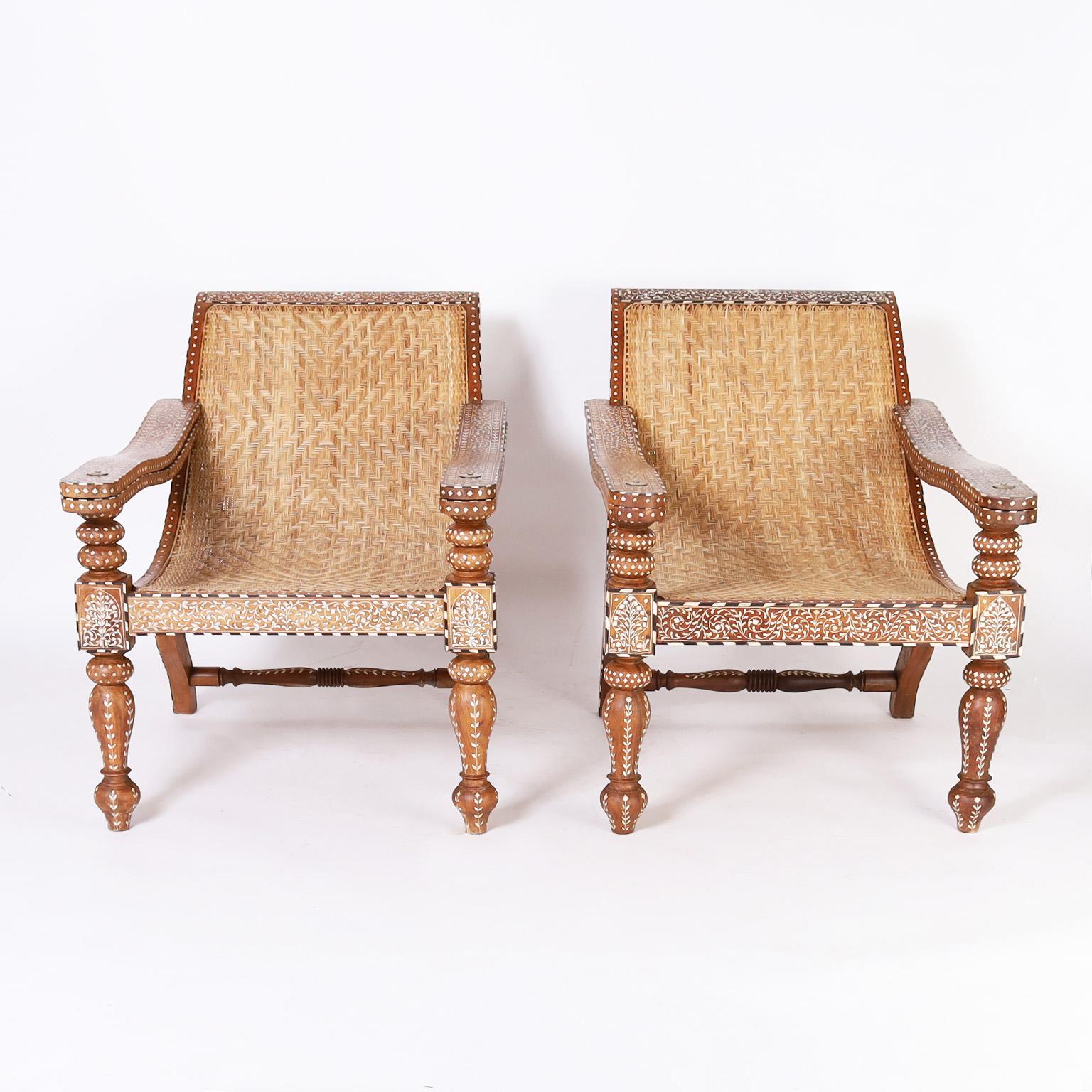 Vintage pair of Anglo Indian plantation chairs crafted in mahogany with iconic colonial form featuring caned seats in an unusual herringbone pattern. Elaborate bone and ebony inlays all around with swing out extensions and turned front legs.