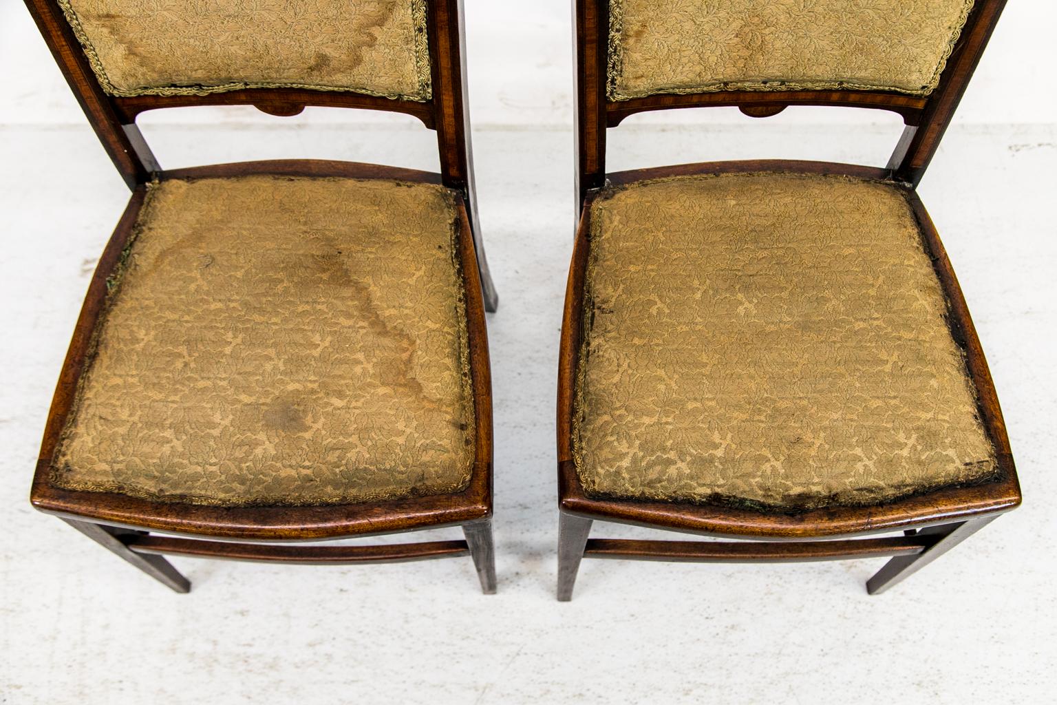 Each inlaid Edwardian chair has a shaped crest rail that is inlaid with boxwood stringing that frames inlaid arabesque panels. The side stiles and cross rails in the back are inlaid with satinwood panels framed with boxwood and ebony line inlays.
