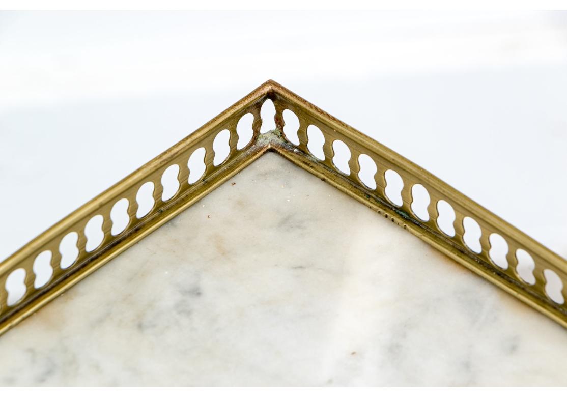 Pair of French corner tables with white marble tops within a raised pieced brass gallery. The tables each with a singular swing out drawer with a brass pull. The table with inlaid tapering legs conjoining with two lower tiers.

Dimensions: 14