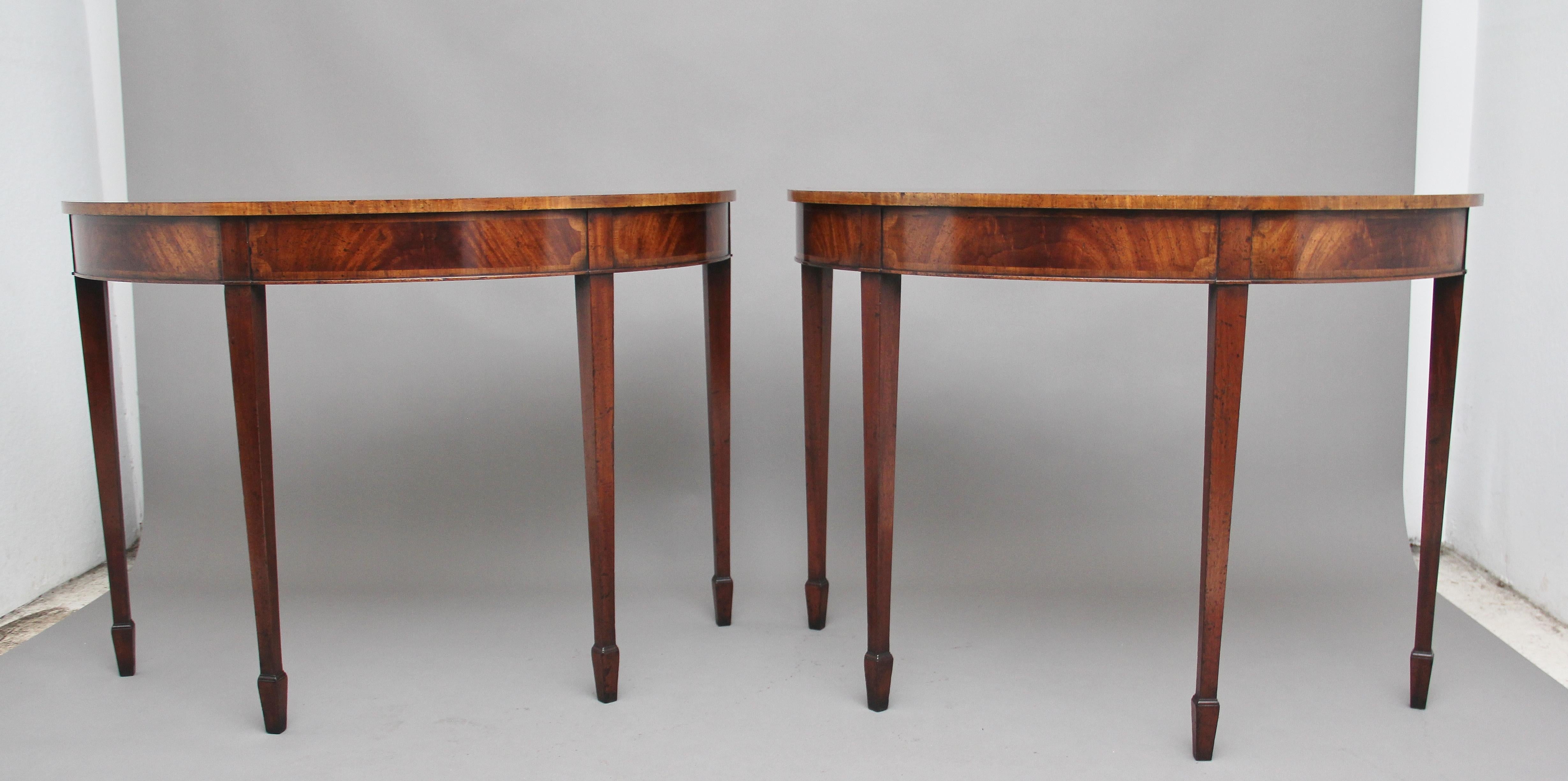 A decorative pair of mid-20th century inlaid mahogany console tables in the Georgian style, the demi lune shaped top crossbanded and having a nice decorative inlaid pattern to the edge, the frieze below is also inlaid, supported on four square