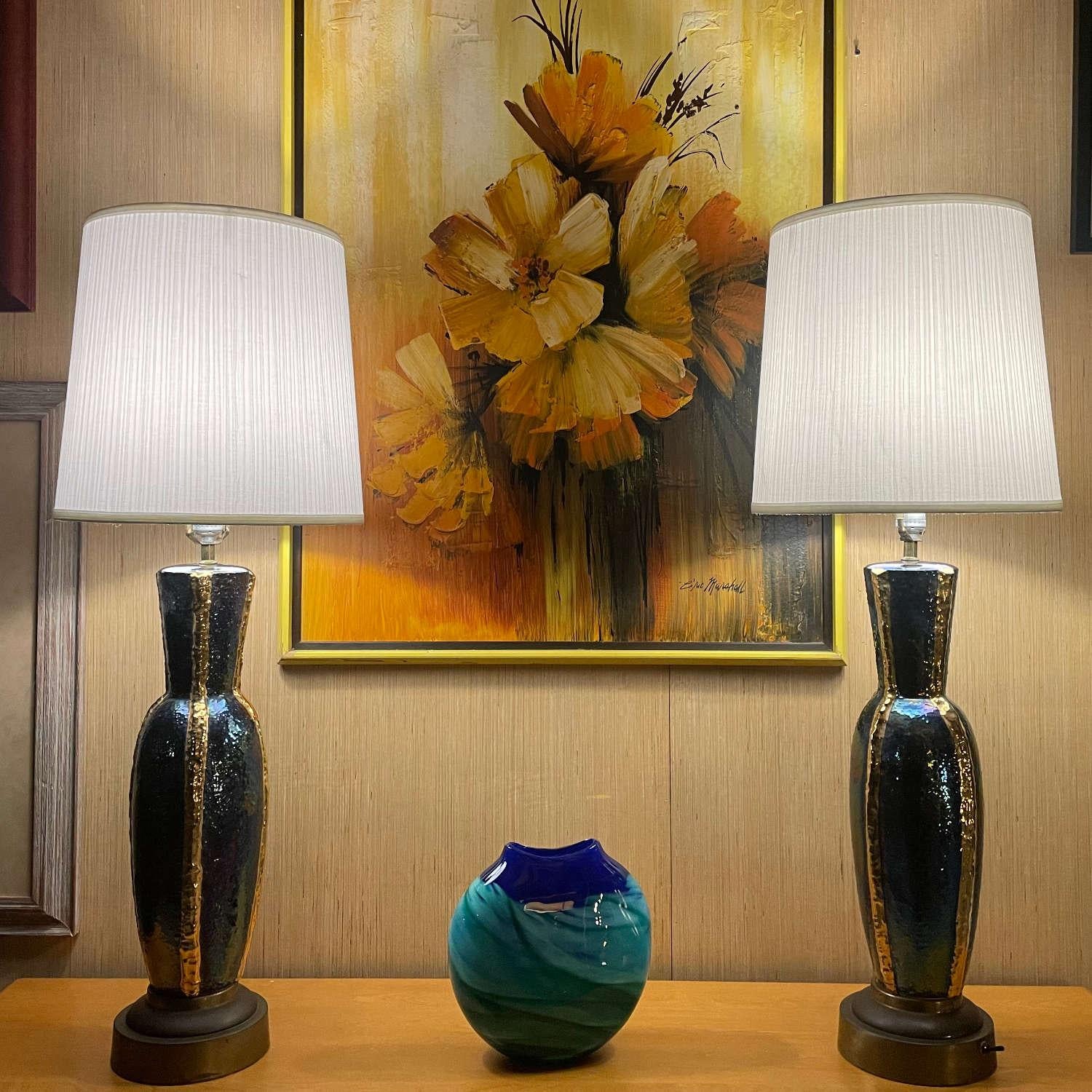Paar blau und gold schillernde Mid-Century Modern Tischlampen. Die eleganten Lampen scheinen ihre Farbe zu ändern, wenn das Licht mit der Keramikglasur spielt. Metallische Goldbänder verlaufen vertikal durch die urnenförmigen Lampen. Oben auf jeder