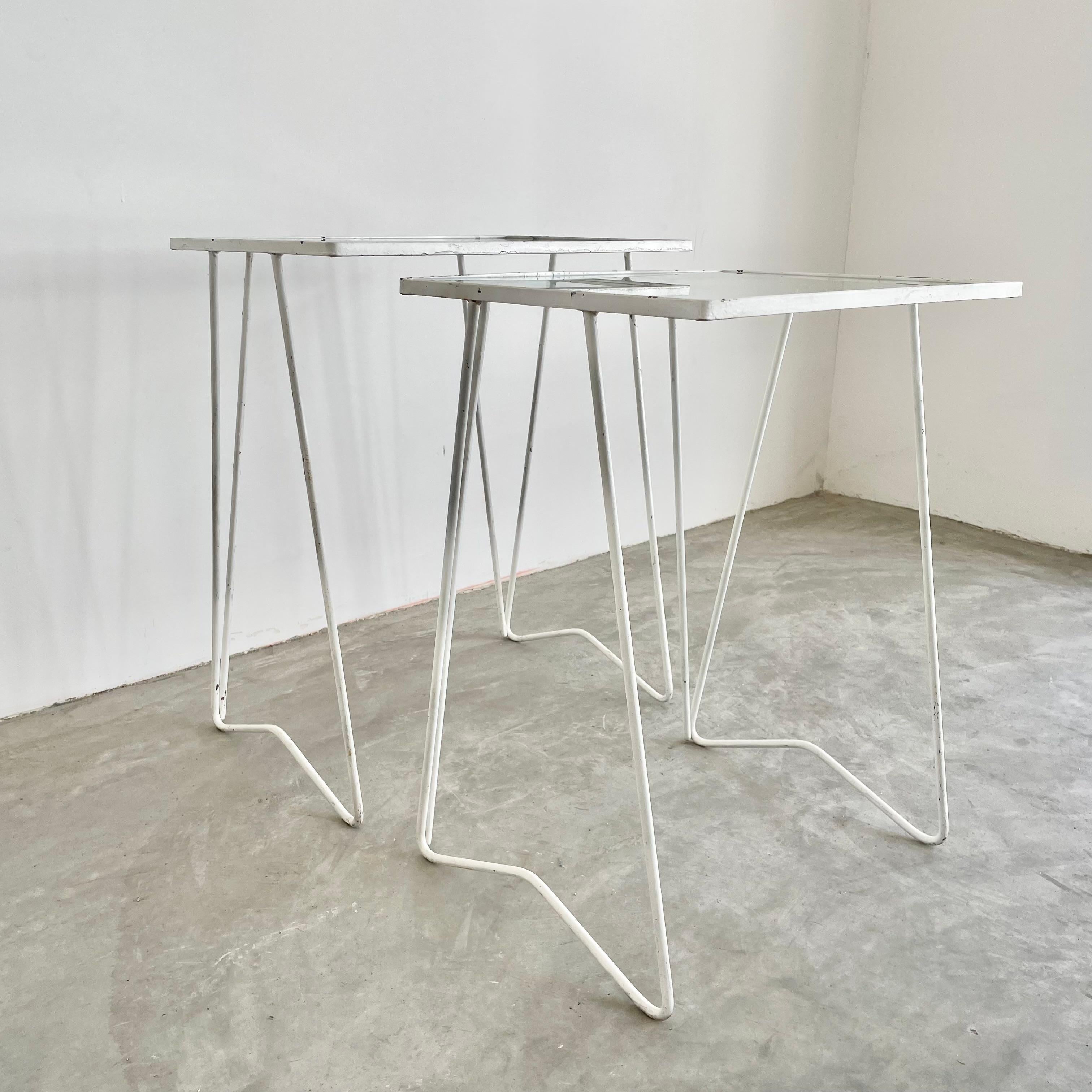 Classic pair of 1970s iron and glass nesting tables. Solid iron frame painted white with hairpin style legs and a glass table tops. Square tables look great stacked together or apart. Tables are in good vintage condition. Perfect cocktail tables for