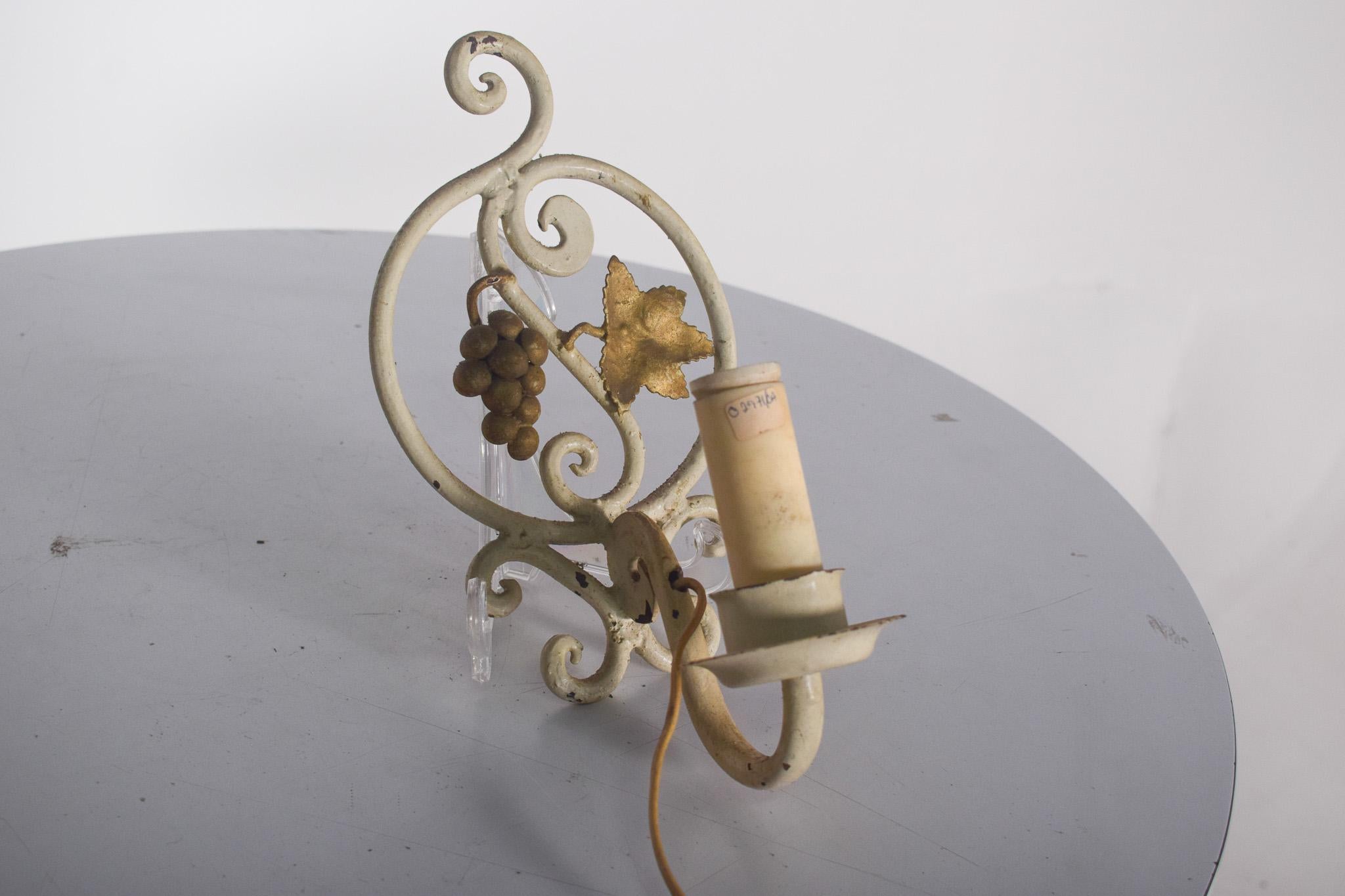 Coppia di applique in ferro e metallo, con grappolo d'uva e vite. Questi pezzi hanno un design classico, con una struttura arrotondata dipinta in crema e arabeschi che trasmettono un tocco elegante e romantico. I dettagli decorativi in metallo