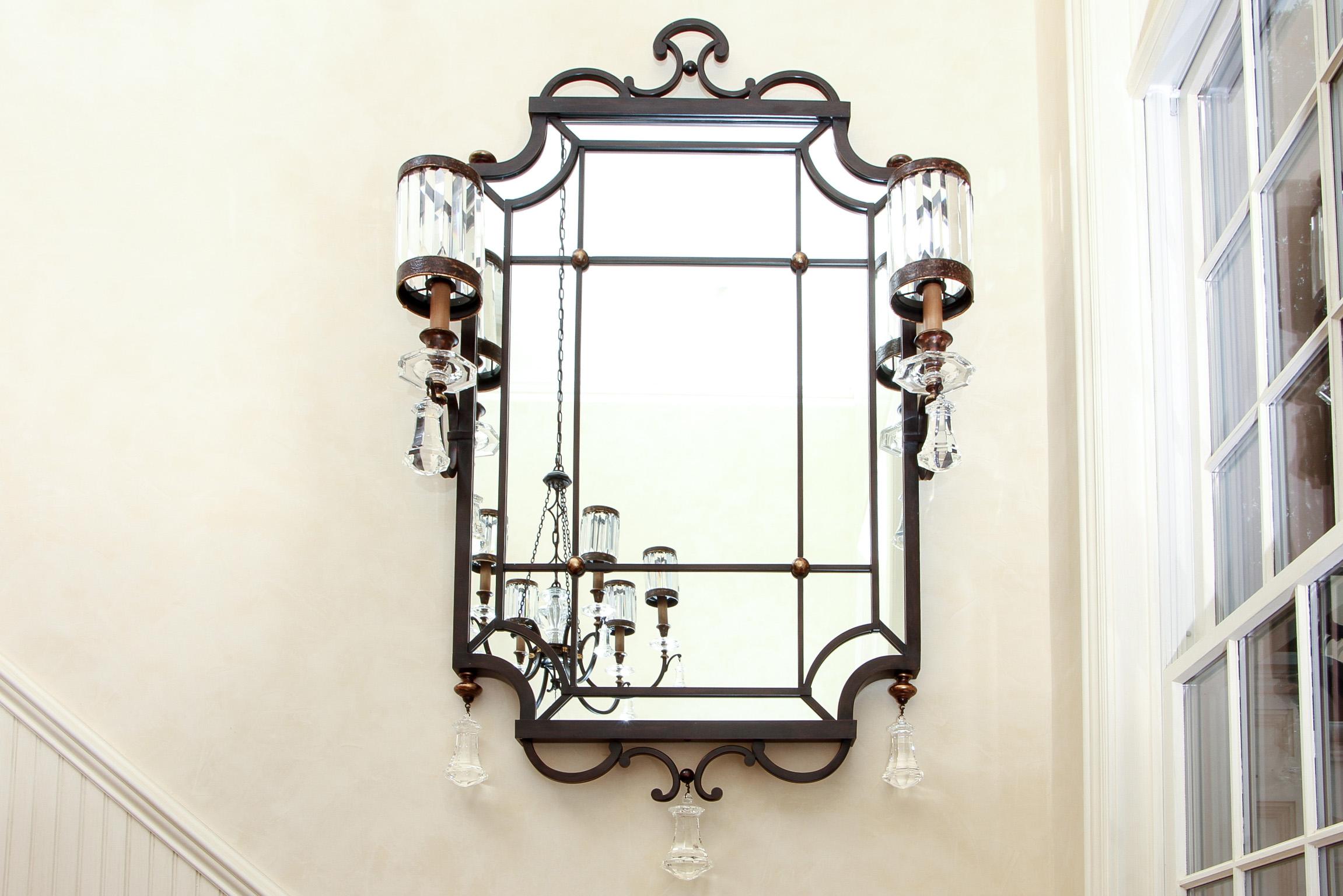 Pair of iron, brass and crystal sconce mirrors, iron frames with scrolled crests and terminals and bras finials and bosses. Two scrolled electrified candle sconces with inset faceted crystal circular shades and faceted crystal bobeches. Cut crystal