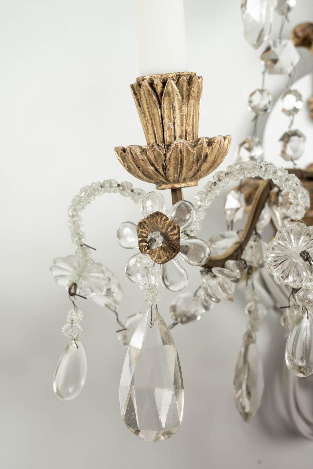 Coppia di appliques in ferro, cristallo e legno dorato intagliato del 1920-1939 circa. Tre bracci su ogni applique ospitano luci singole a candelabro, per un totale di sei. Cablato di recente per l'uso negli Stati Uniti. La piastra posteriore di