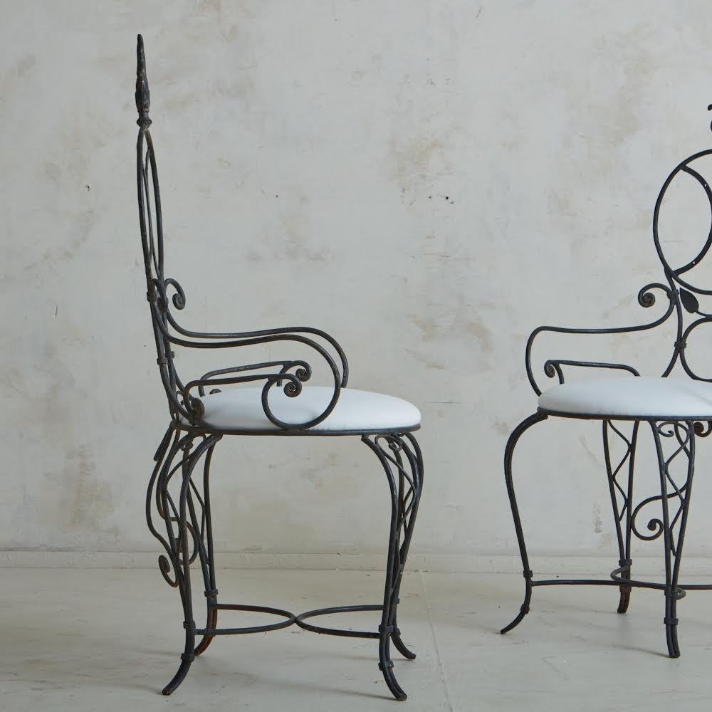 Ein Paar französischer Esszimmerstühle im Vintage-Stil mit komplizierten schmiedeeisernen Rahmen mit eleganten Schnörkeln, Blattmotiven und einer X-Stange. Diese Stühle haben runde Rückenlehnen mit dekorativen Endstücken und stehen auf geschwungenen