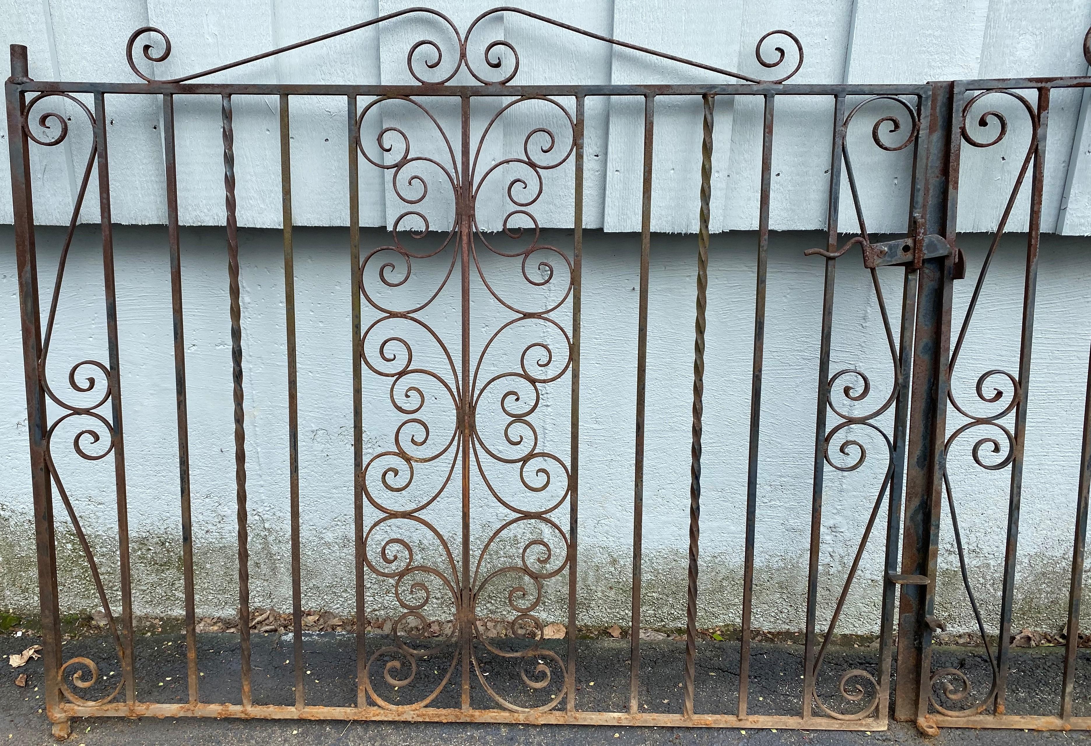 A fine pair of ebonized iron gates, probably from a driveway or road entrance, with scrollwork and rope twist design and latch intact, probably dating to the 20th century in good overall condition, with some surface rust and buildup mostly along the