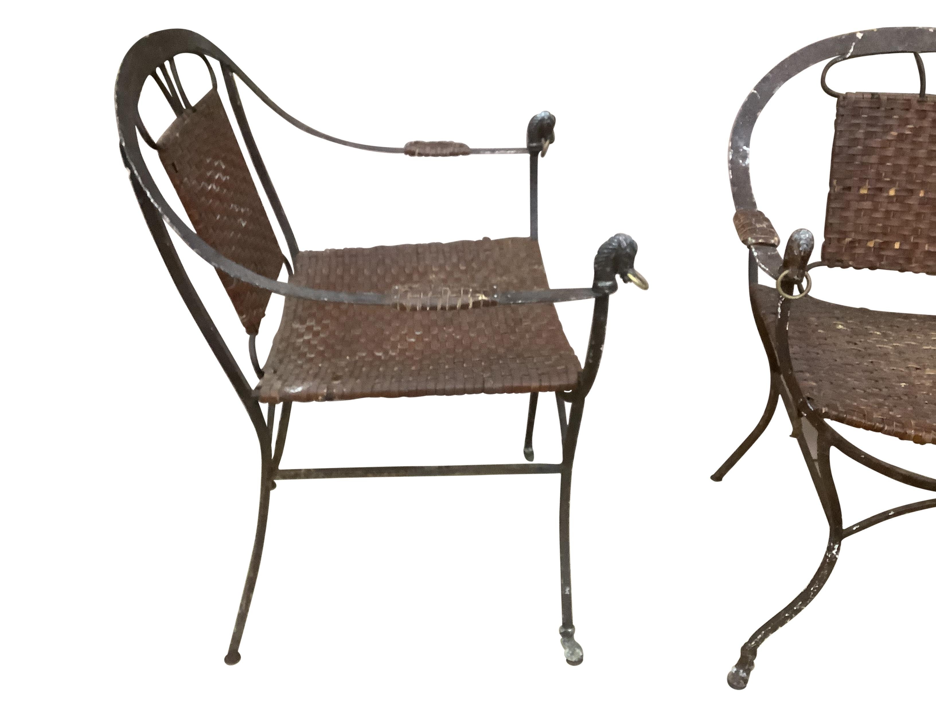 Pair of Iron Horseshoe Back and Leather Chairs. Hand hammered iron in an antique brown finish. Seats and arm rests arm are in leather in a woven webbed design. Arm terminate with a stylized horse head with a brass ring. The legs of the chairs shade