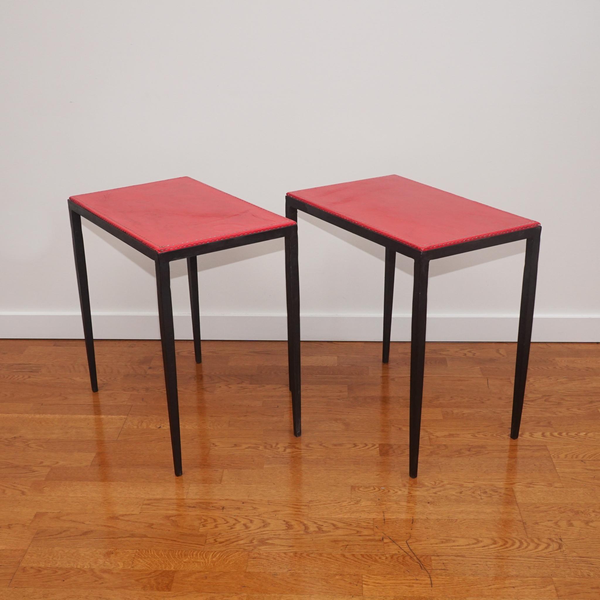 The pair of iron side tables, shown here, are in the style of Jean-Michel Frank. 
Featuring lean, tapered legs and a red leather top with contrast stitching, the side tables are not only distinctive and stylish, but perfectly scaled to sit