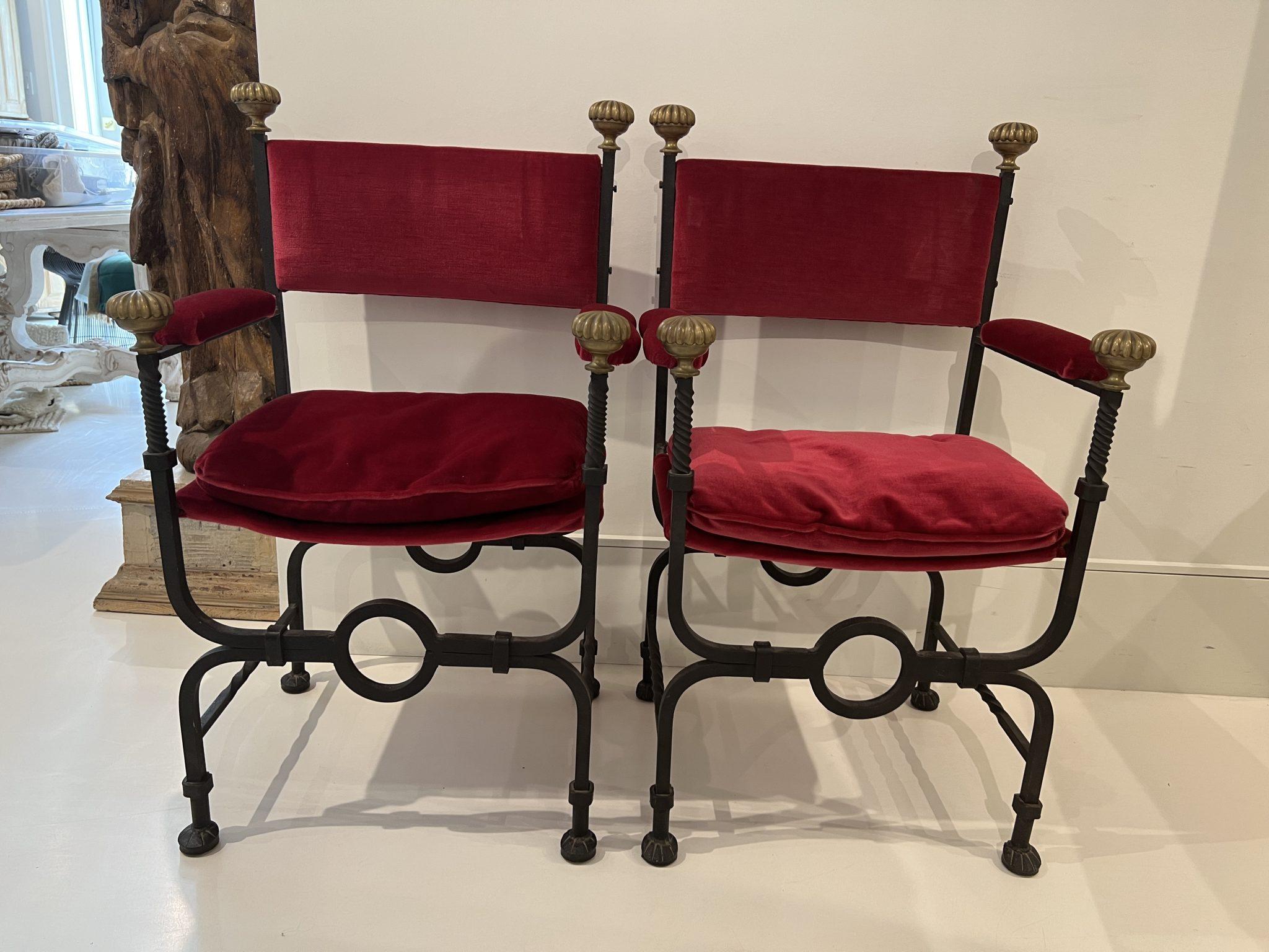 A pair of Savonarola chairs fabricated in heavy iron with brass embellishments. The seats, arms and back are upholstered in lush red velvet.