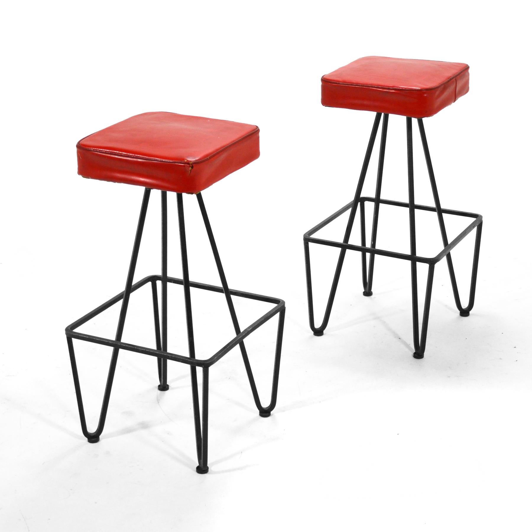 These two handsome stools have a great graphic quality and are built to last. They have bases of solid square stock iron and upholstered seats (the seats show their age and will likely need restoration). They are very reminiscent of the work of