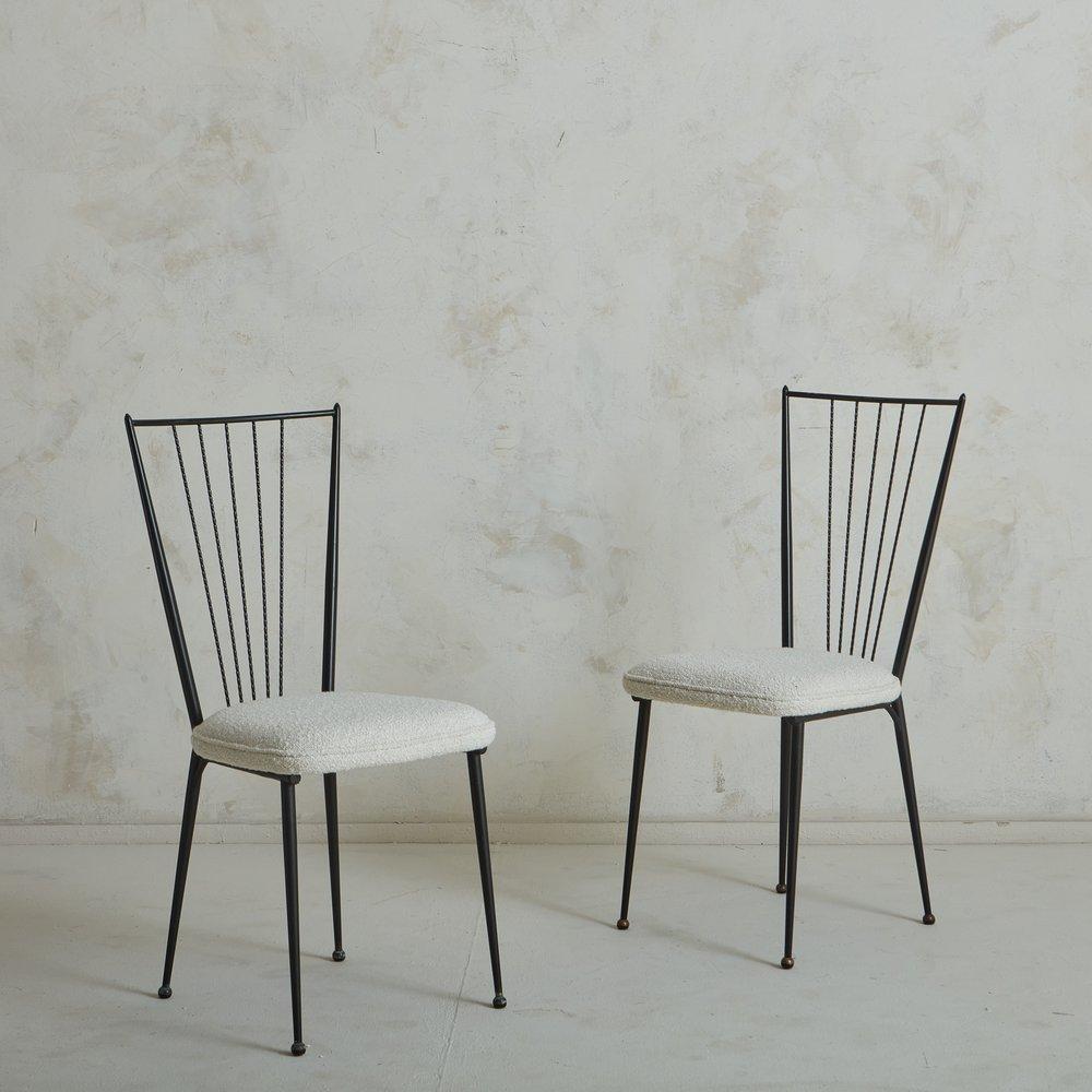 A pair of 1950s French dining chairs in the style of Colette Guedon. These chairs feature sleek iron frames with ladder backs and petite ball feet. They were newly reupholstered in elegant white wool. Unmarked. Sourced in France, 1950s.
