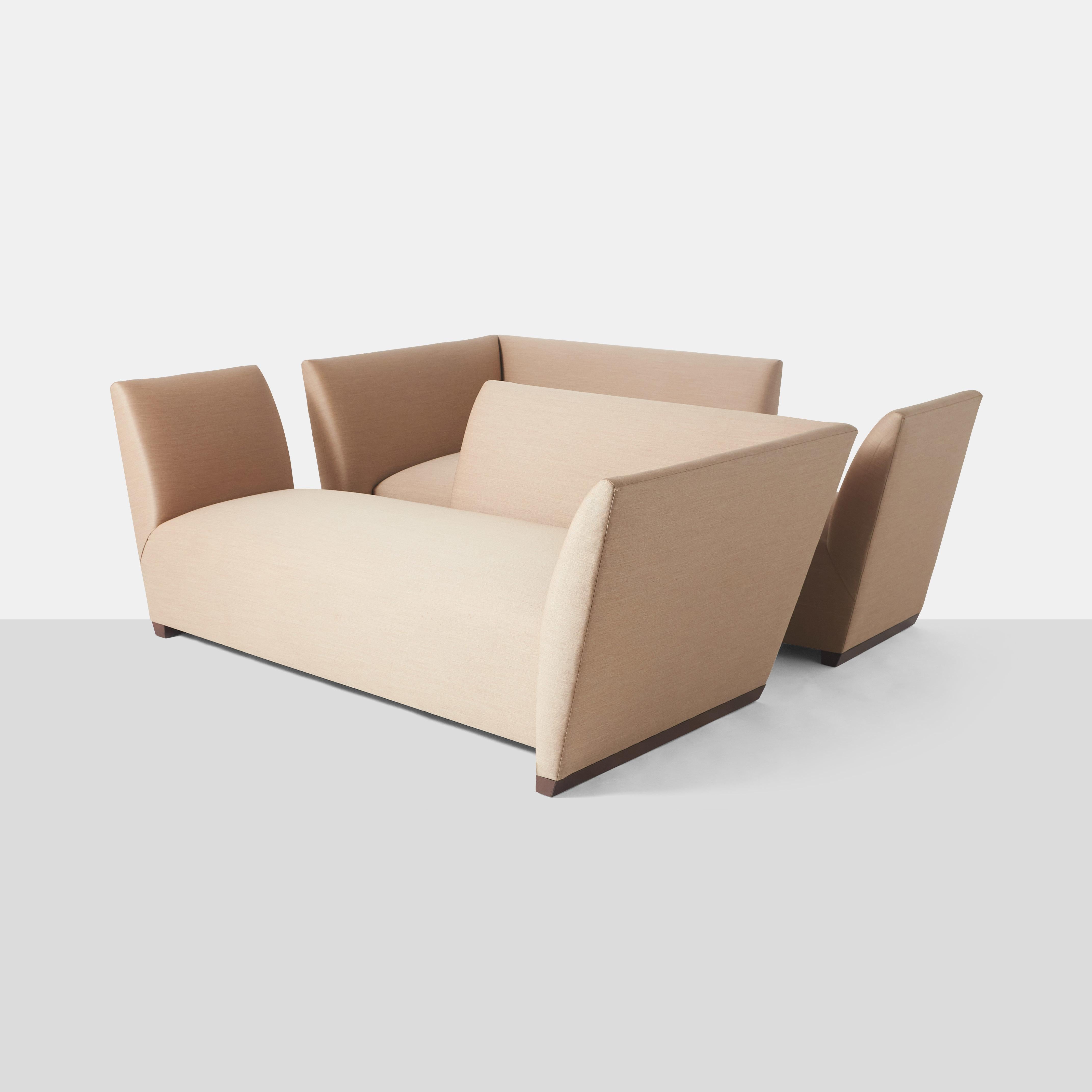 A pair of sculptural island sofas designed by Joe D'Urso for Donghia. Retains original Donghia label. The wood base is in good condition and there are no holes or tears to the pale beige upholstery. There is some wear and fraying on one corner of
