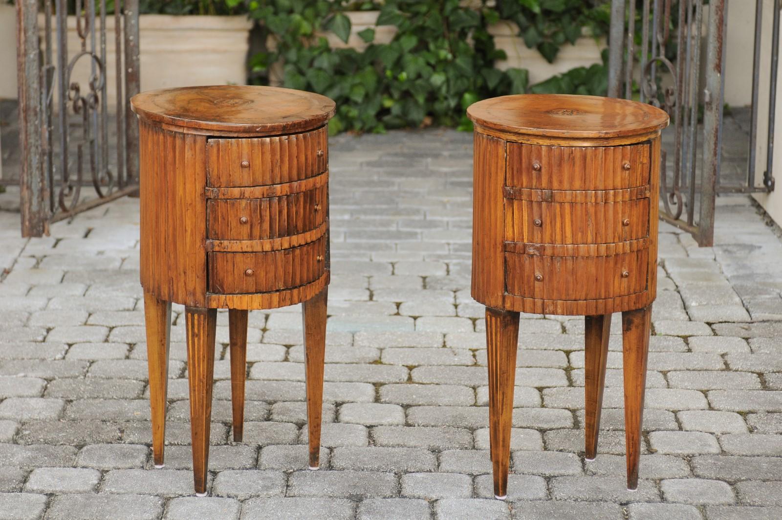 A pair of Italian neoclassical end tables from the early 19th century, with marquetry decor, three drawers, fluted accents and tapered legs. Born in Italy during the early years of the 19th century, each of this pair of exquisite end tables features