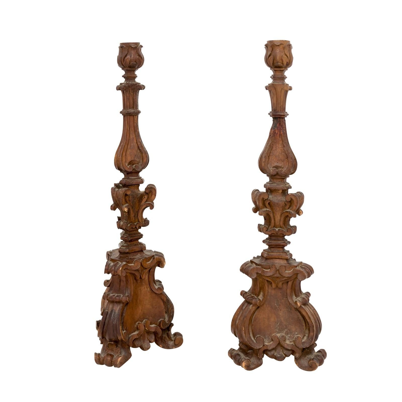 A pair of Italian Baroque period carved wooden candlesticks with acanthus leaves, volutes, carved scrolling feet and great rustic character. Featuring a pair of Italian Baroque period carved wooden altar candlesticks, effortlessly radiating an air