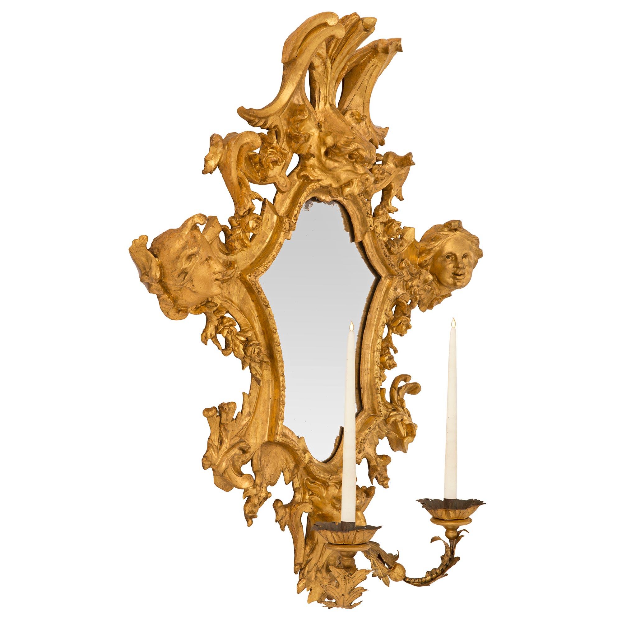 A stunning and rare pair of Italian 17th century Baroque period giltwood Roman mirrored sconces. Each two arm sconce retains its original mirror backplate framed within an elegant and most decorative mottled border and richly carved wrap around