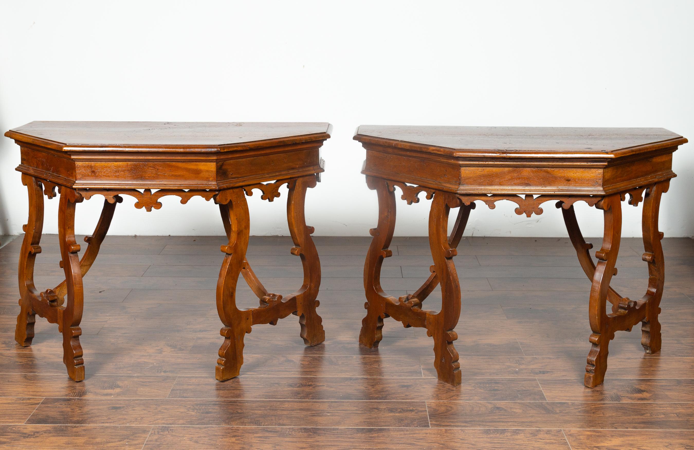 A pair of Italian walnut demilune tables from the mid 1800's  with polygonal tops and lyre base. Born in Italy during the mid 1800's , each of these exquisite demilunes features a polygonal top sitting above a stunning base. Lyre shaped legs are