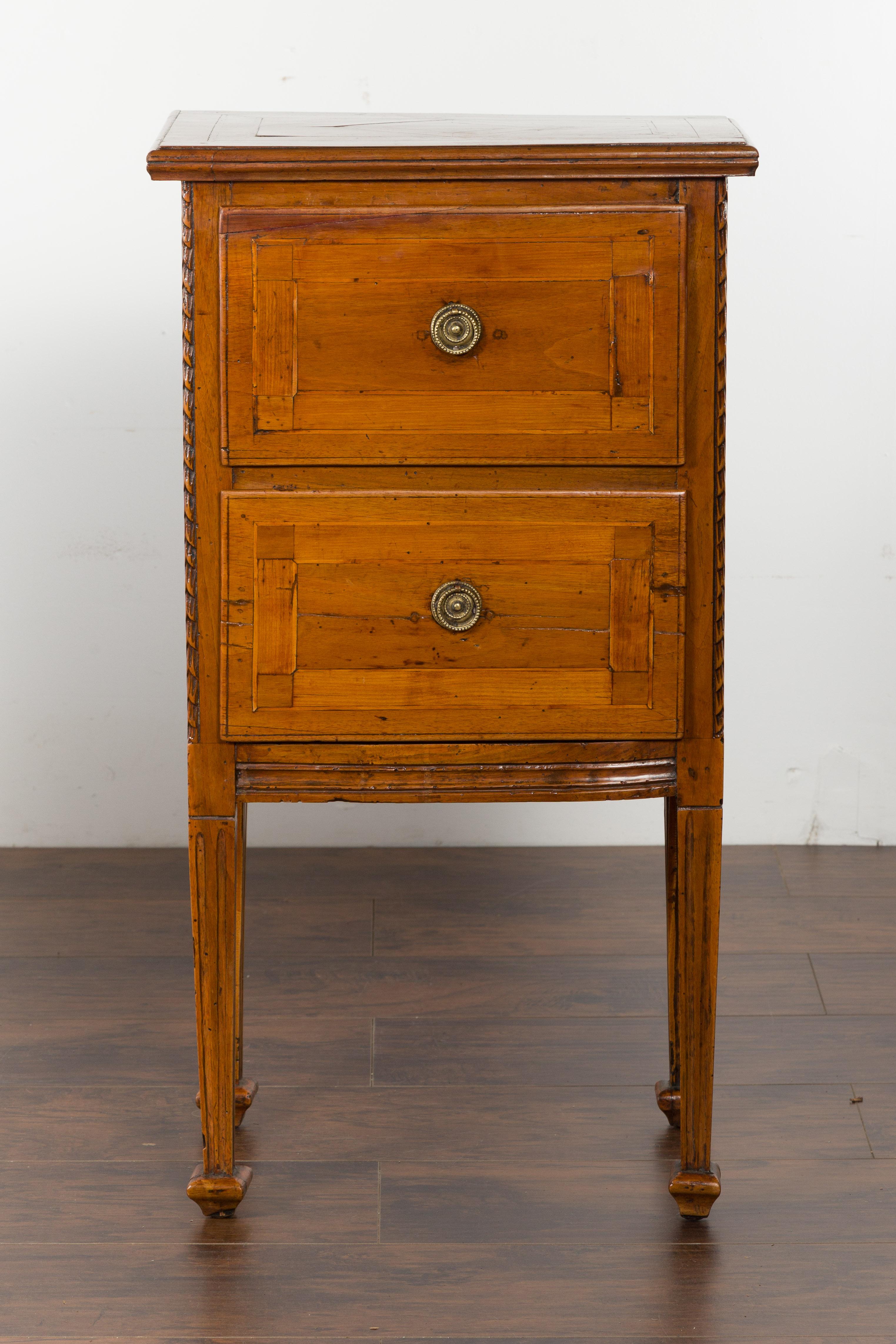 A pair of Italian neoclassical period walnut bedside tables from the early 19th century, with two drawers and tapered legs. Created in Italy during the first quarter of the 19th century, each of this pair of walnut bedside tables features a