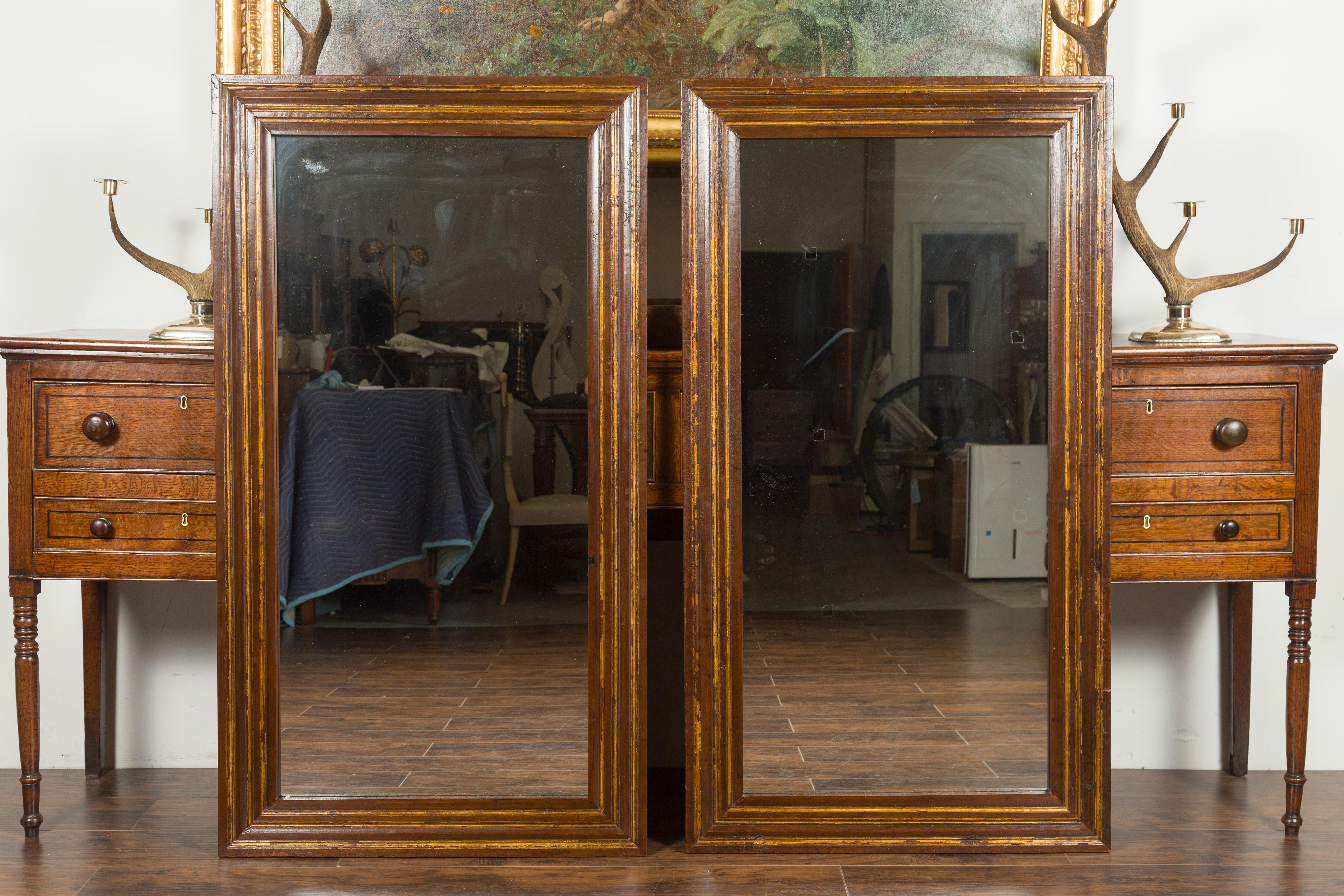 A pair of Italian walnut mirrors from the early 19th century, with brown patina and gilt accents. Created in Italy during the first quarter of the 19th century, each of this pair of walnut mirrors features a simple, rectangular frame, alternating