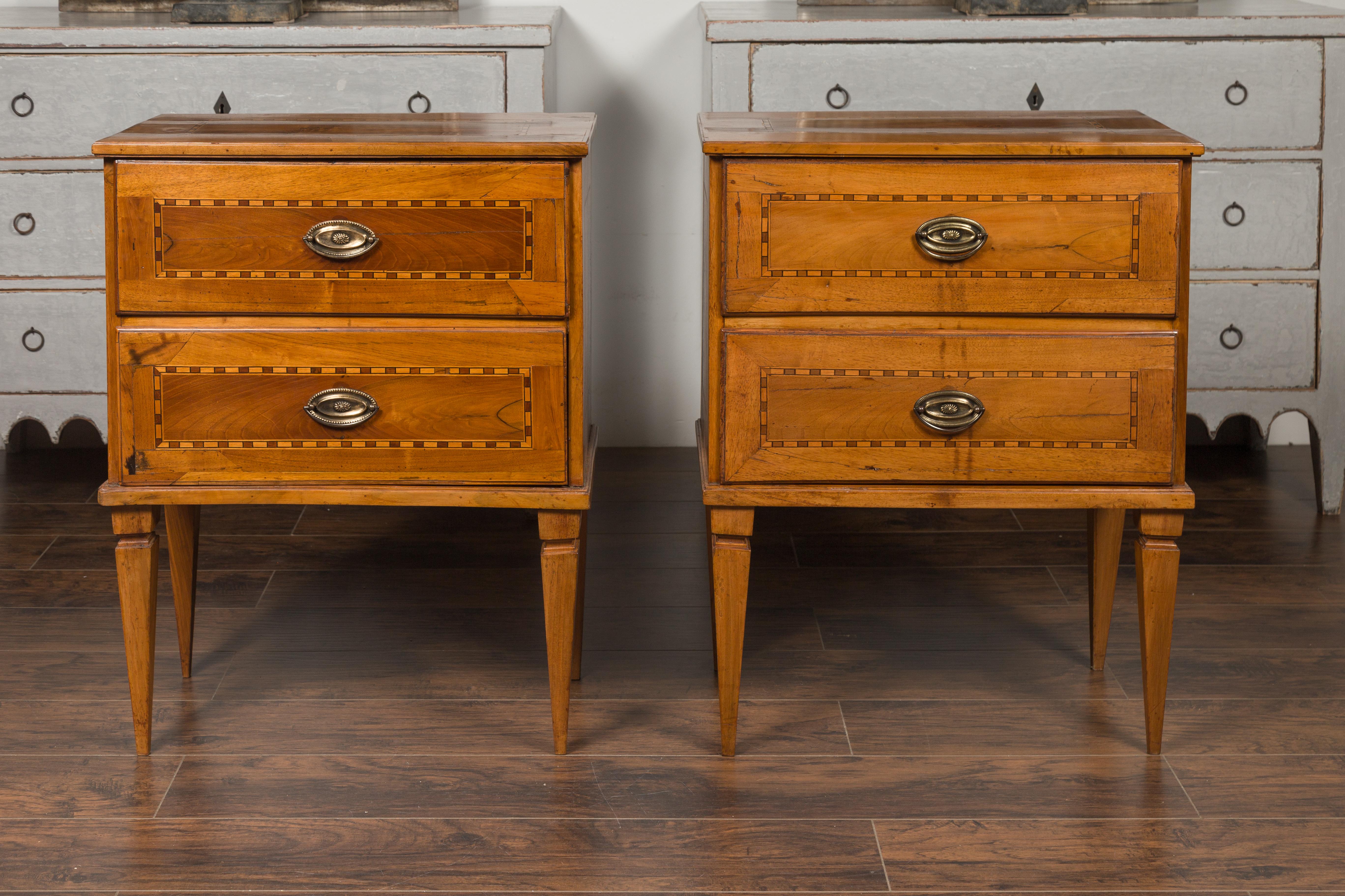 A pair of Italian neoclassical style walnut commodes from the mid-19th century, with two drawers, inlay and tapered legs. Born in Italy during the 1850s, each of this pair of petite commodes features a rectangular top sitting above two drawers,