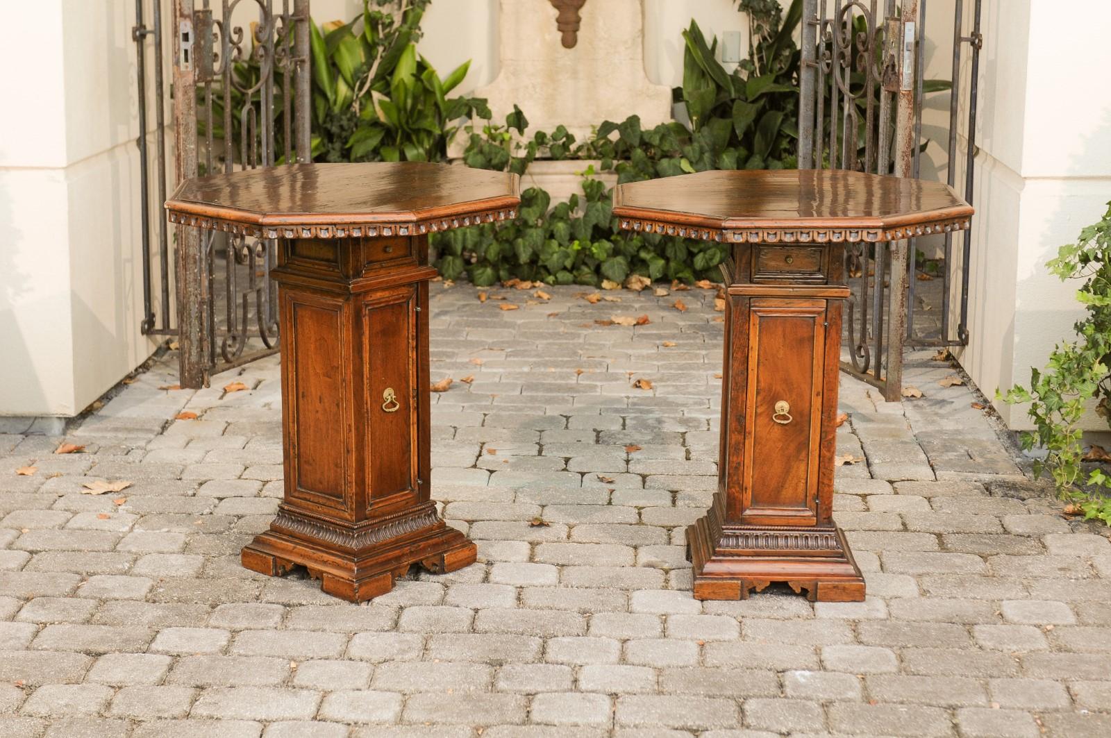 A pair of Italian octagonal walnut pedestal end tables from the mid-19th century, with single-door and drawer. Born in Italy during the mid-19th century, each of this pair of walnut tables features an octagonal top adorned with carved scoop patterns