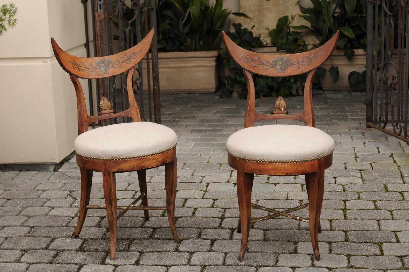 A pair of Italian side chairs from the mid-19th century, with crescent shaped backs, new linen upholstered seats and saber legs. Born in Italy during the third quarter of the 19th century, each of this pair of unusual Italian chairs features a