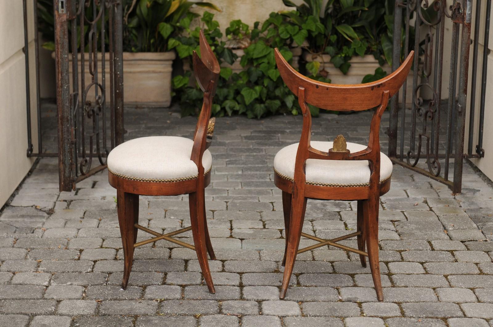 A pair of Italian side chairs from the mid-19th century, with crescent shaped backs, new linen upholstered seats and saber legs. Born in Italy during the third quarter of the 19th century, each of this pair of unusual Italian chairs features a