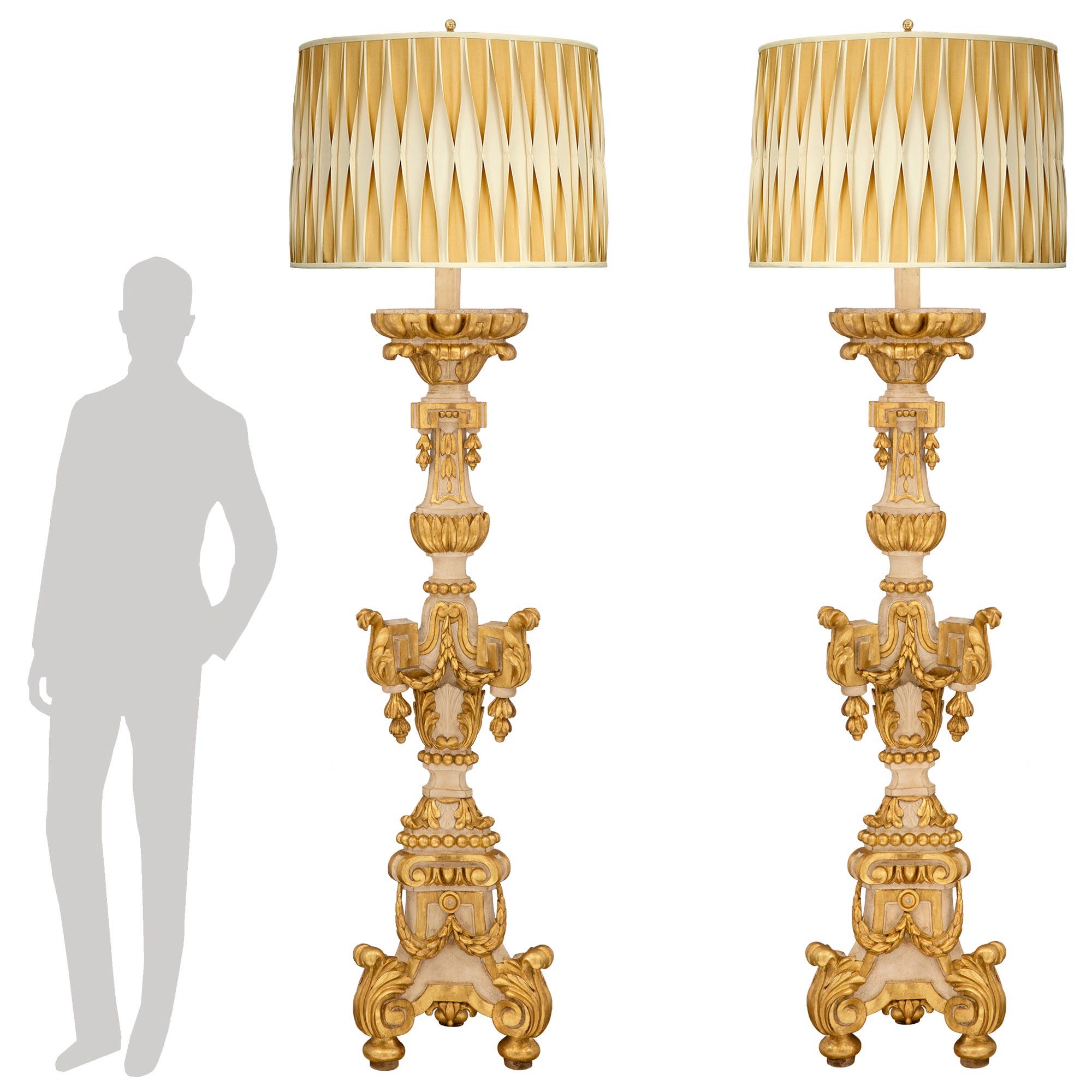 A magnificent and very large scale pair of Italian 18th-century Baroque period patinated and giltwood floor lamps. Each statement-making torchière floor lamp is raised by elegant tope-shaped feet with large acanthus leaves at the triangular base