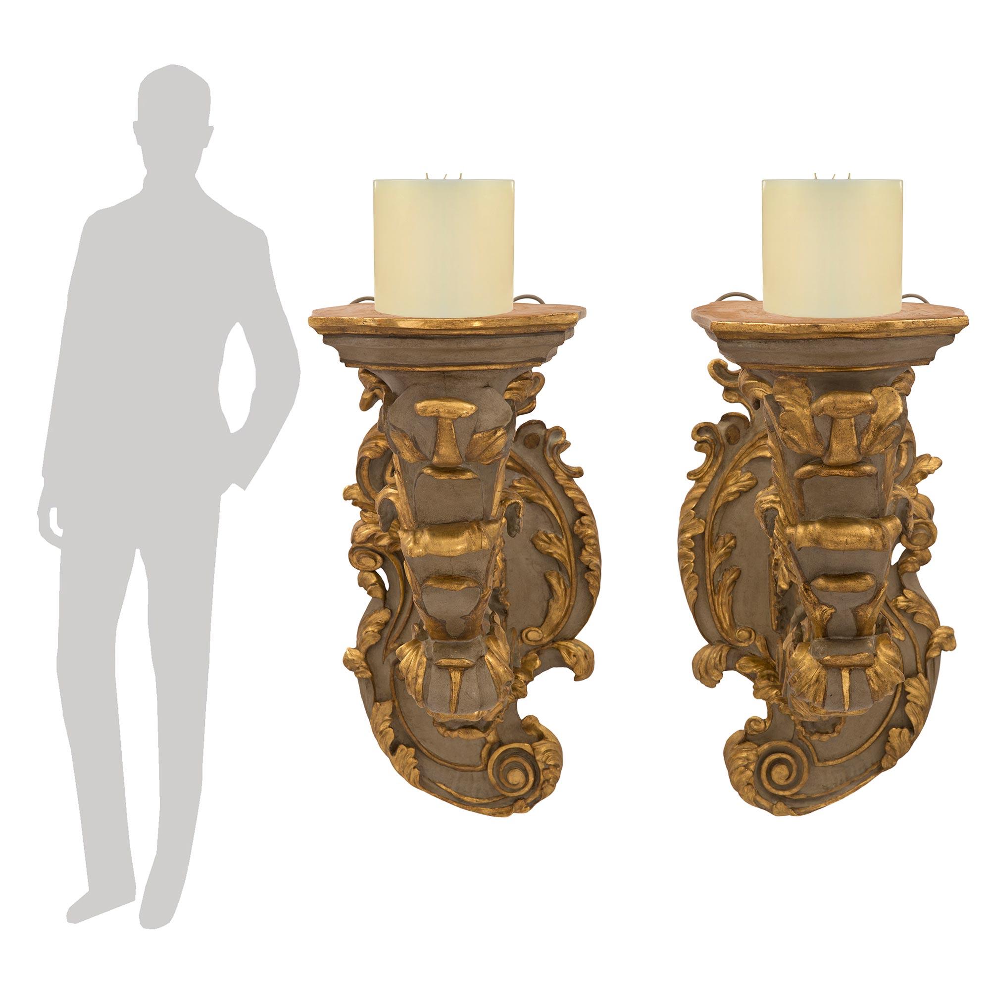 Une superbe et très impressionnante paire d'appliques en bois patiné et doré de la période baroque du 18e siècle. Chaque applique est centrée par une belle plaque de fond très décorative aux motifs feuillus richement sculptés et aux accents dorés.