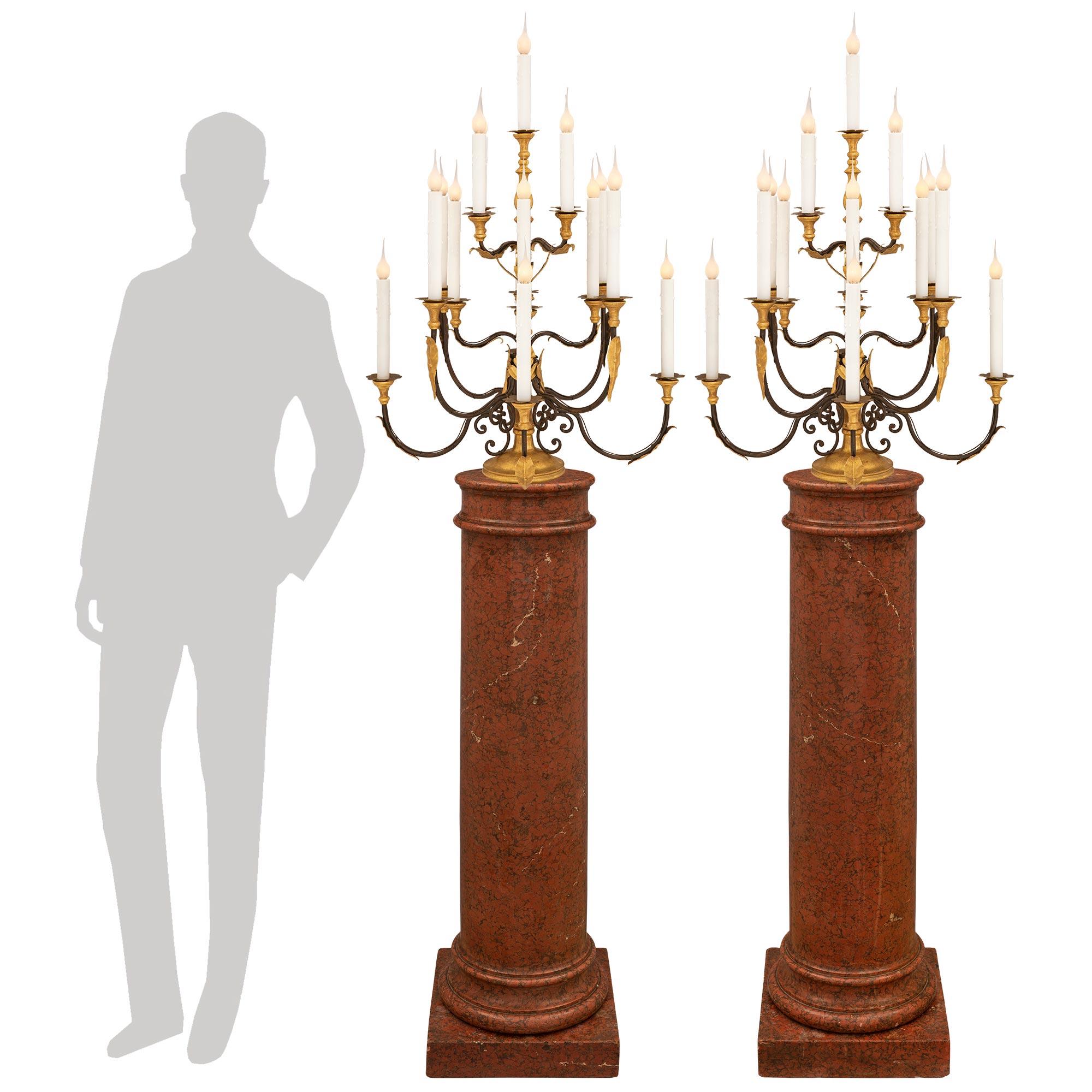 A beautiful pair of Italian 18th century Baroque st. wrought iron, giltwood and pressed gilt metal candelabra lamps. Each seventeen arm lamp is raised by an elegant circular giltwood base with a fine wrap around mottled border. Each of the wrought