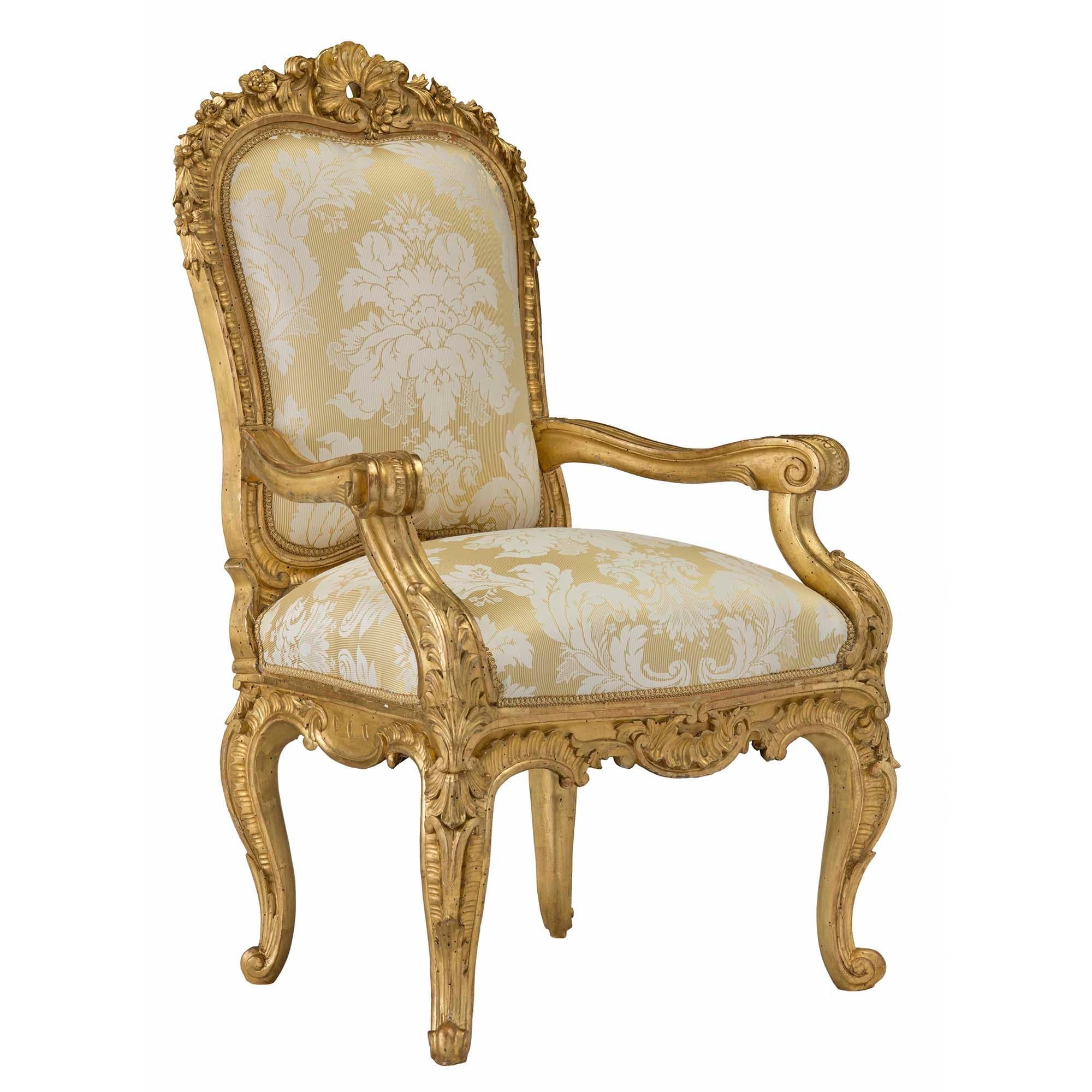 A pair of magnificent and high quality Italian 18th century Louis XV period Roman giltwood throne armchairs. Each finely carved chair is raised on cabriole legs accented with large acanthus leaves. The scrolled frieze is decorated with a large